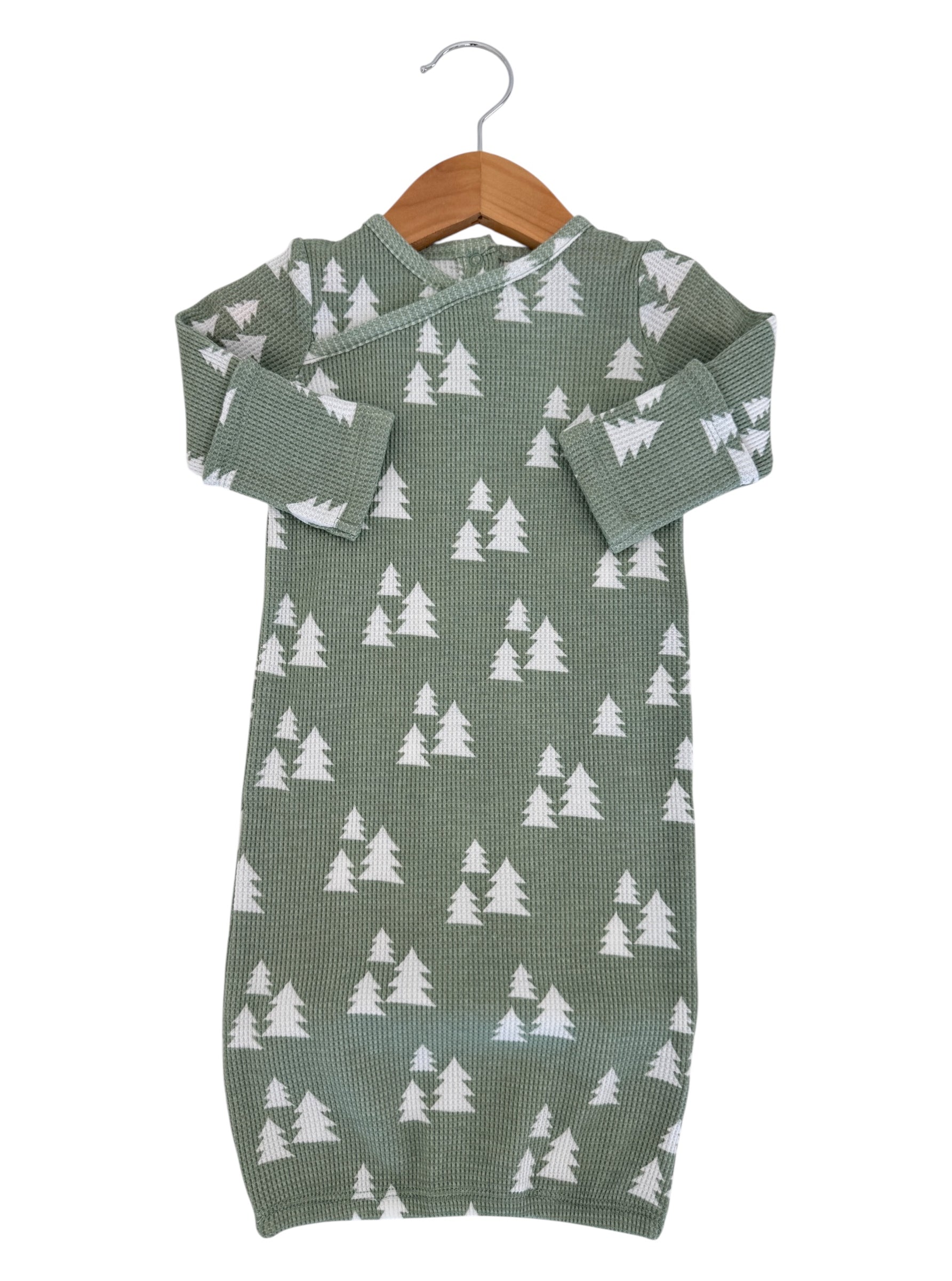 Green infant outfit with white tree pattern, hanging on a wooden hanger against a white background.