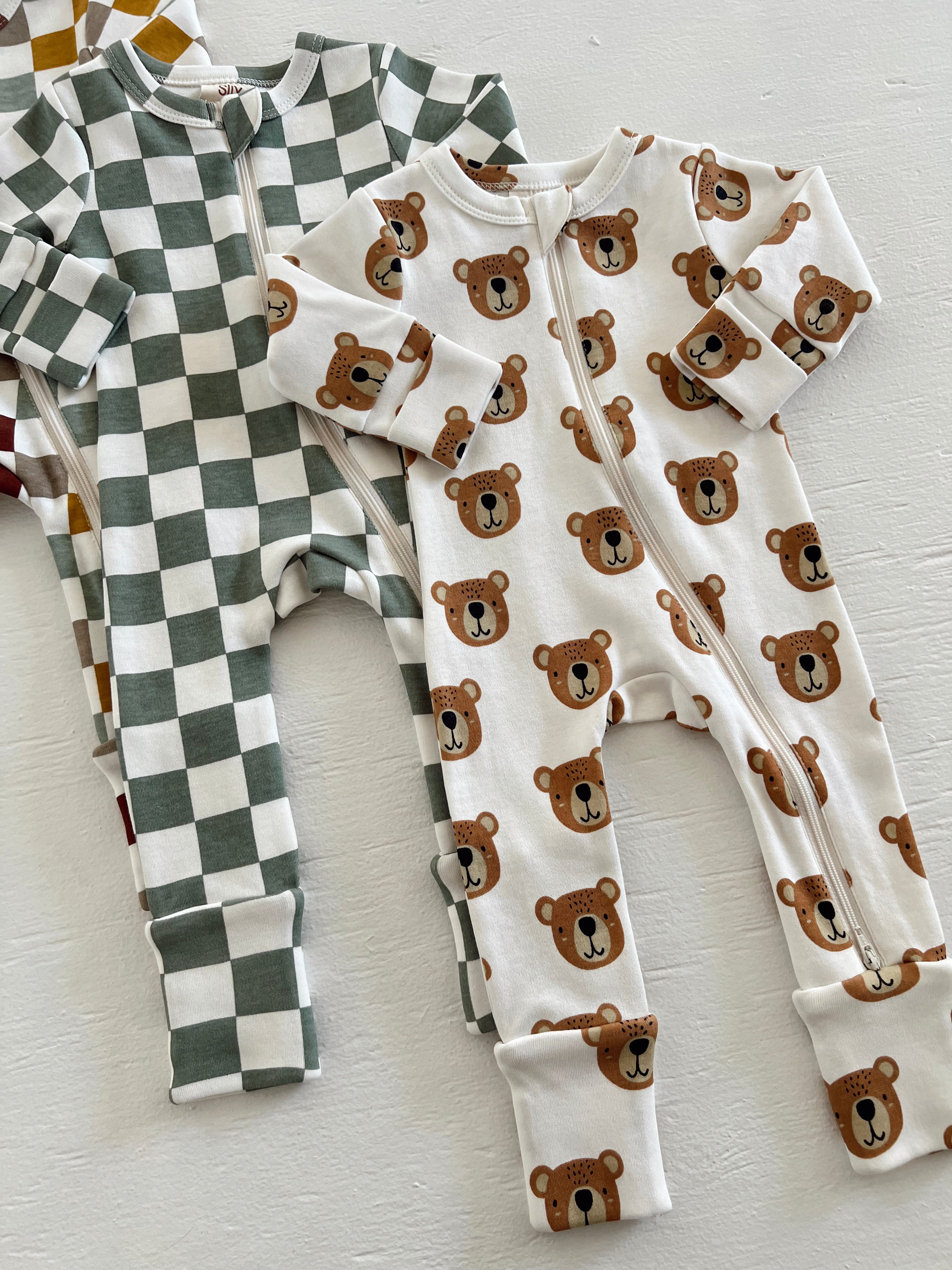 Two baby onesies featuring a green checkered pattern and a white bear print on a textured white background.