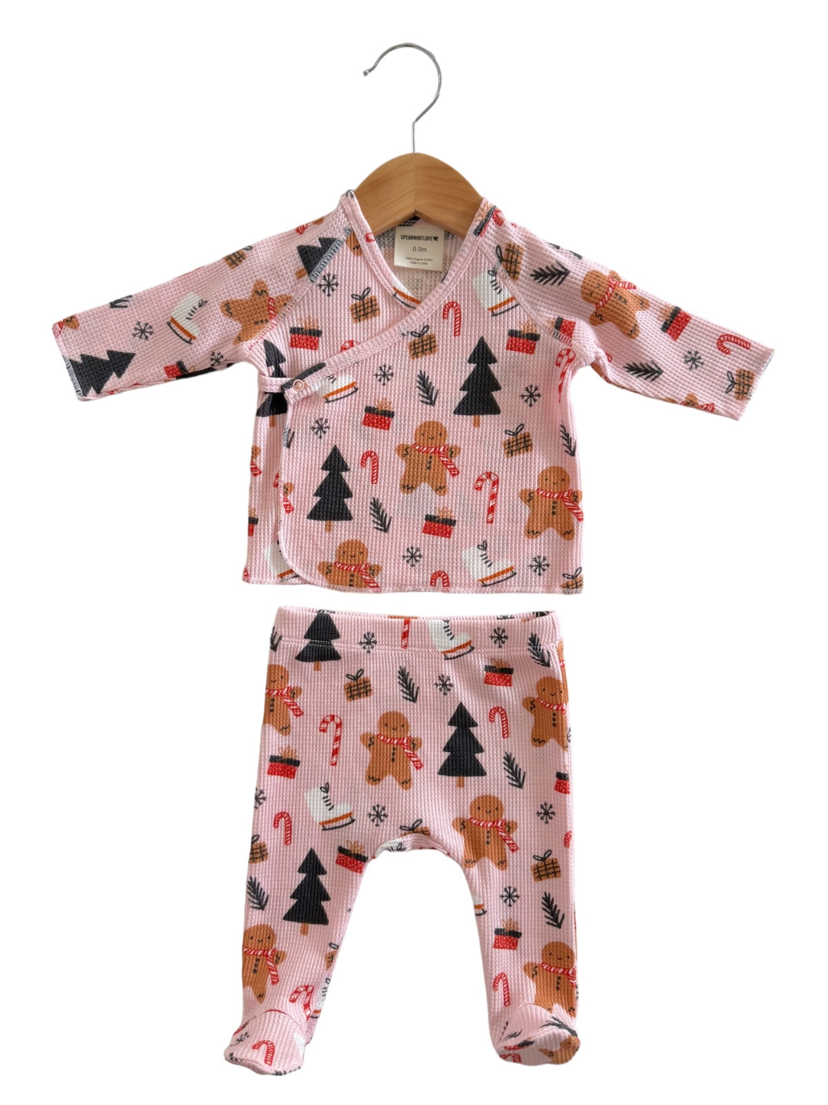 Pink baby outfit with gingerbread, candy canes, and trees, featuring a wrap top and matching pants.