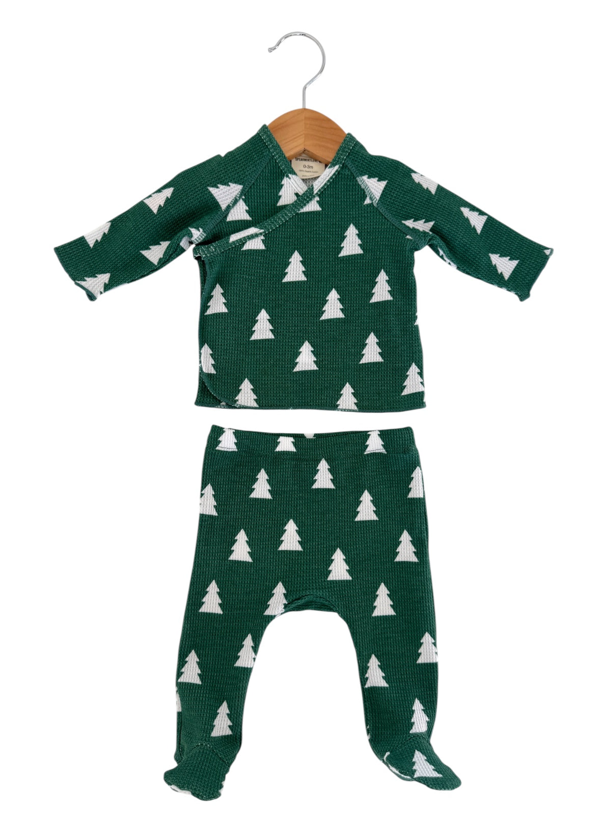 Green baby outfit with white tree patterns, featuring a wrap top and matching pants, hanging on a wooden hanger.
