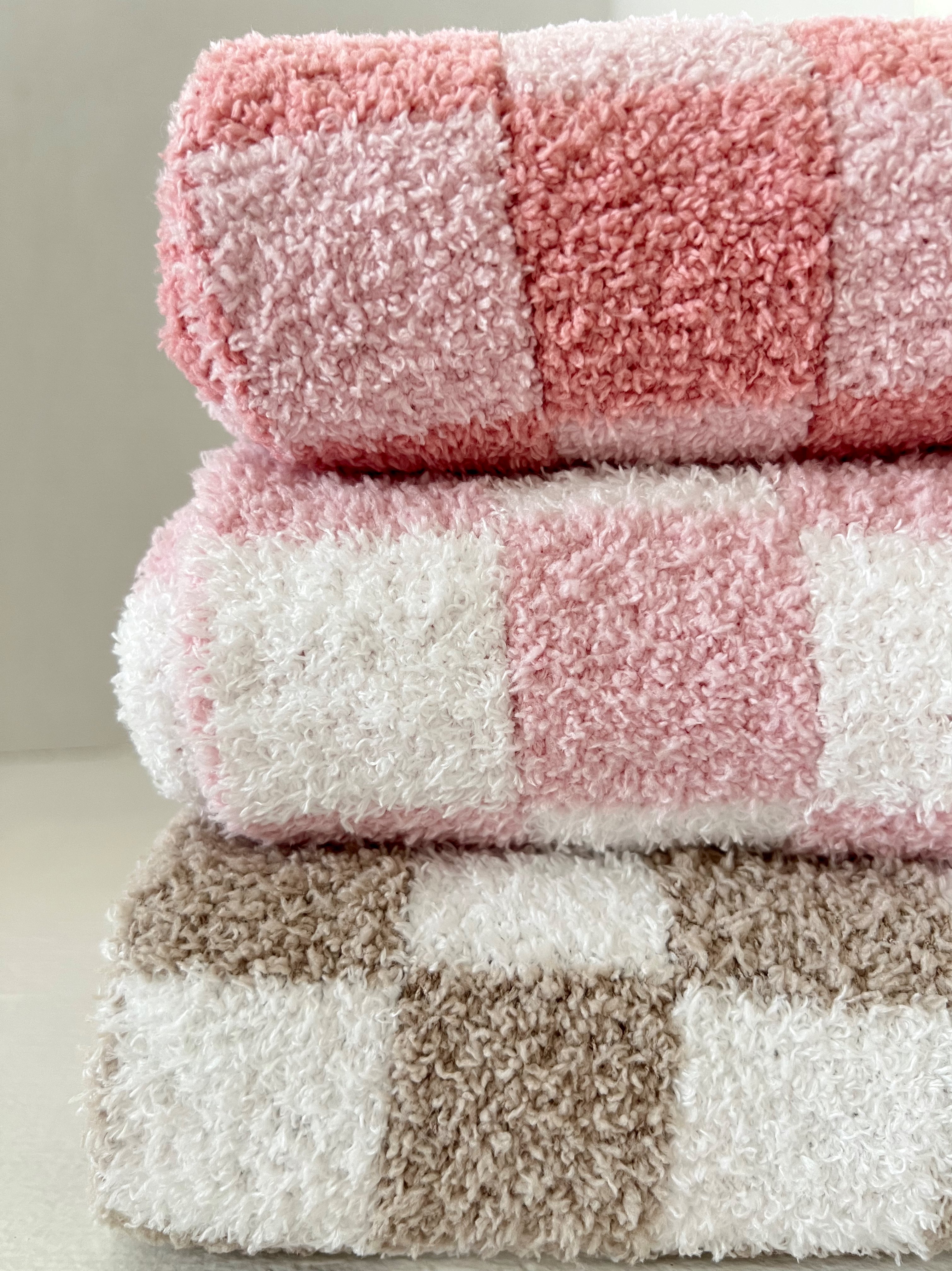 Three stacked towels in pink, white, and tan plaid patterns, showcasing soft textures and bright colors.