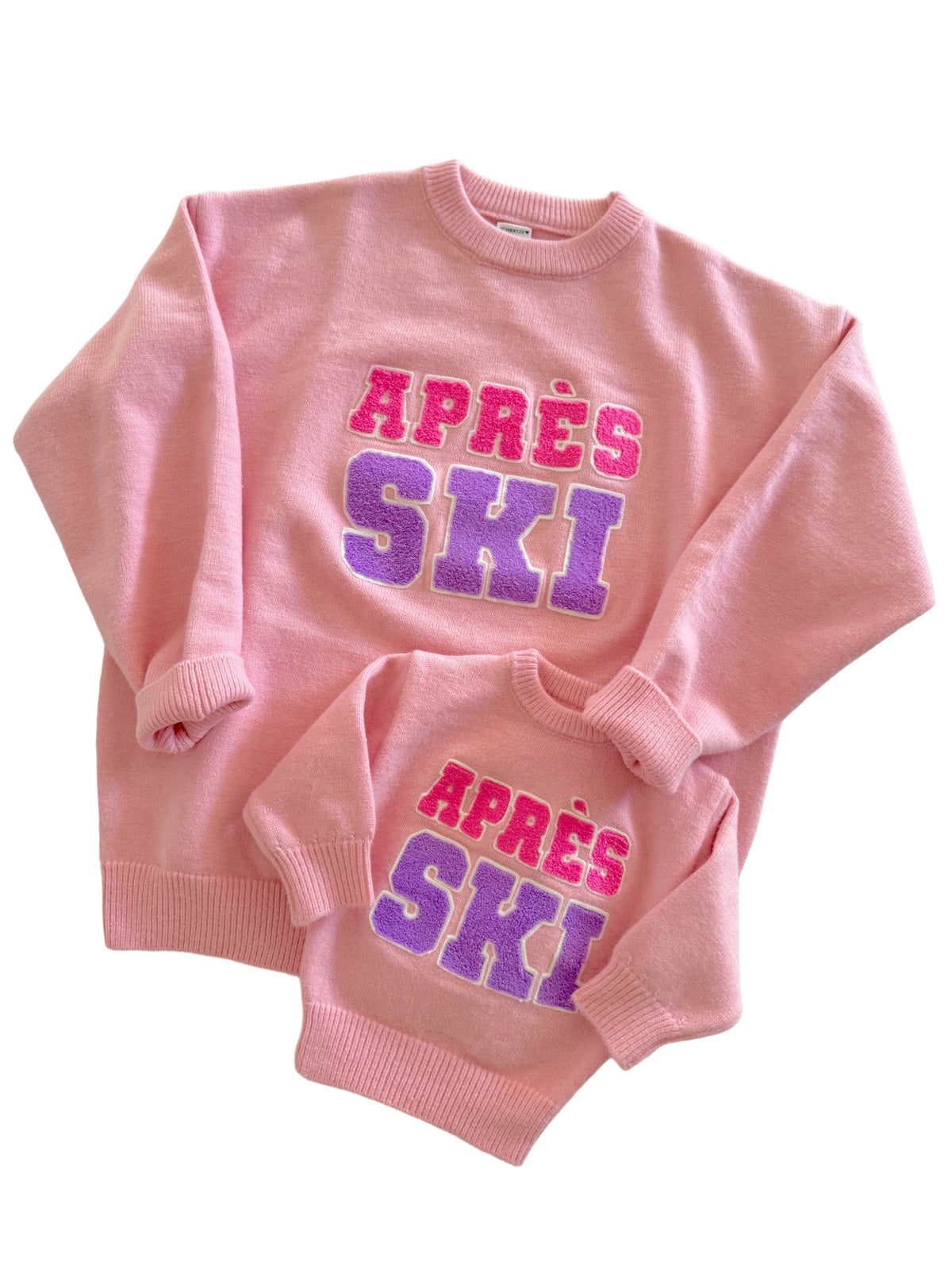 Two matching pink sweatshirts with "APRÈS SKI" lettering in colorful, textured font. One adult and one child size.