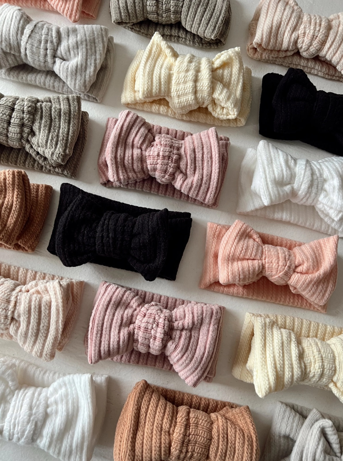 An array of textured bow headbands in various colors, neatly arranged on a light background.