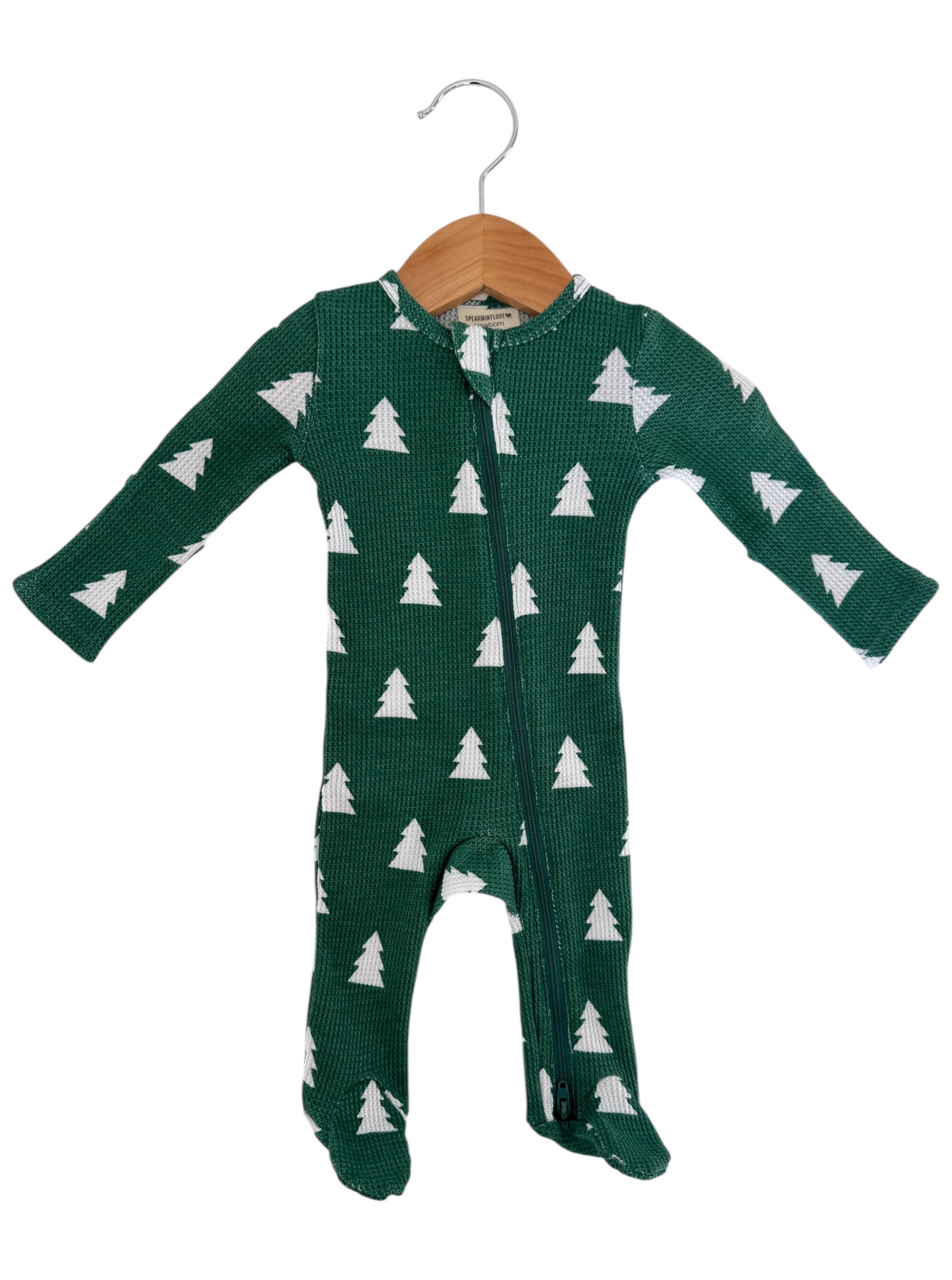 Green baby onesie with white pine tree pattern, featuring a front zipper and long sleeves, displayed on a wooden hanger.