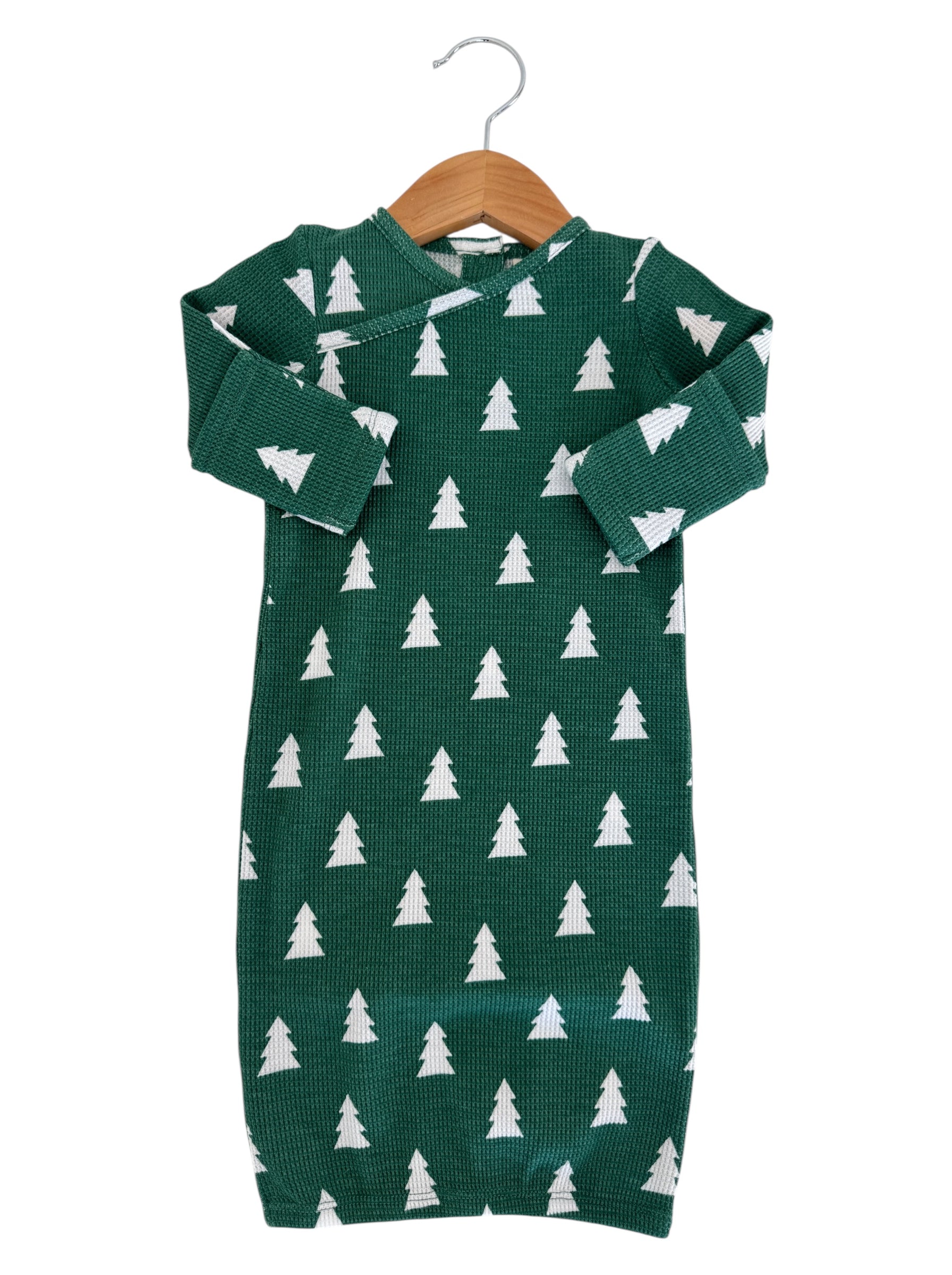 Green infant dress with white pine tree pattern, displayed on a wooden hanger.
