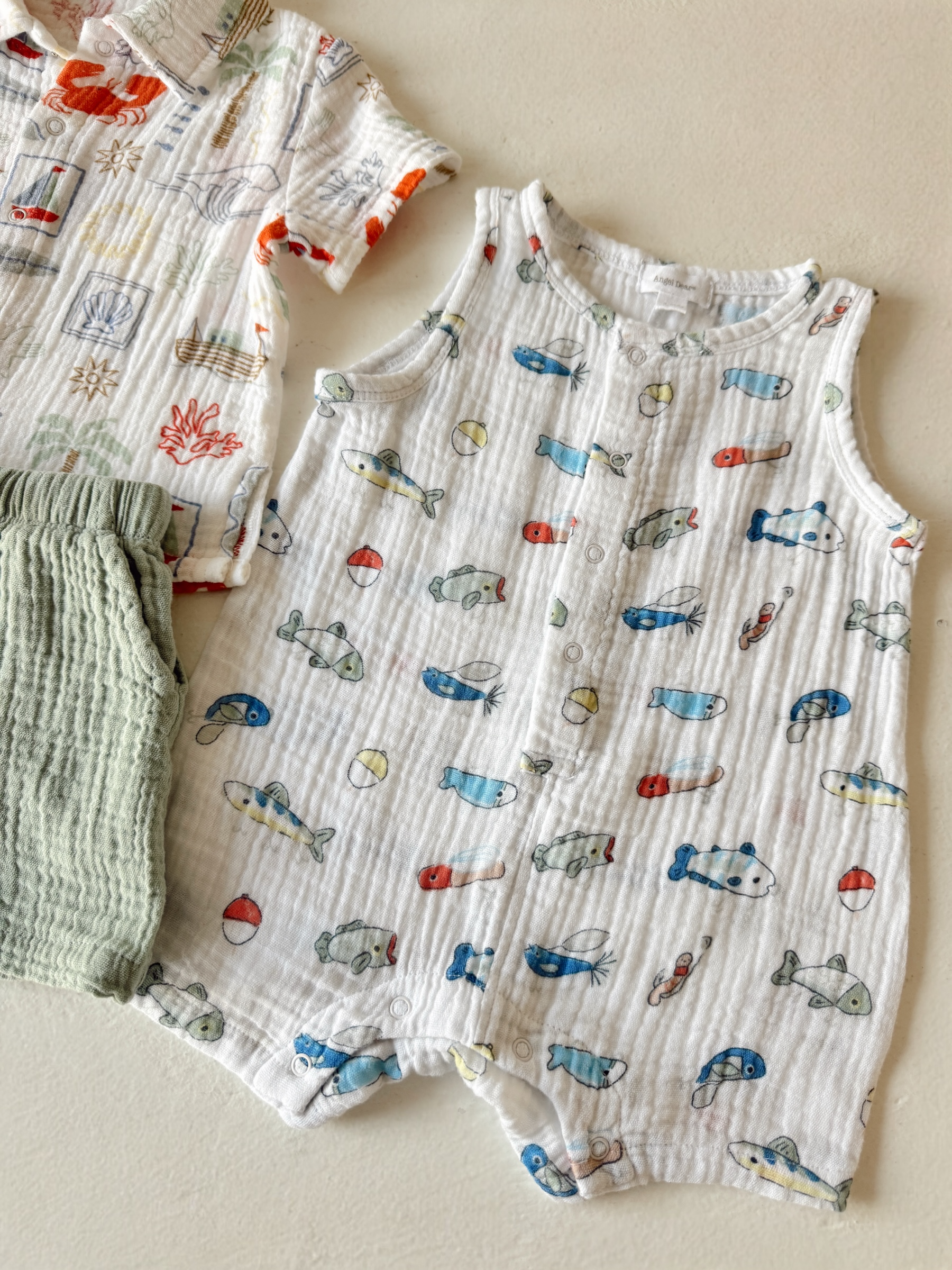 Two baby outfits: a fish-patterned onesie and a short-sleeved shirt with a crab design, laid on a light surface.