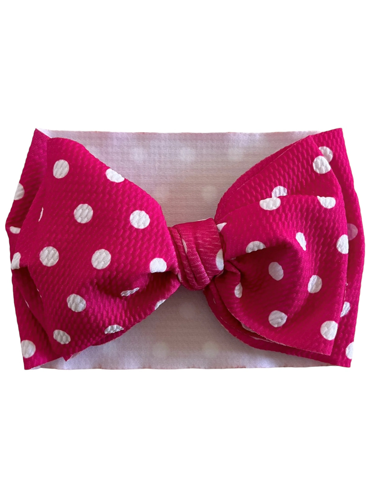 Bright pink headband with large white polka dot bow, set against a soft white background.