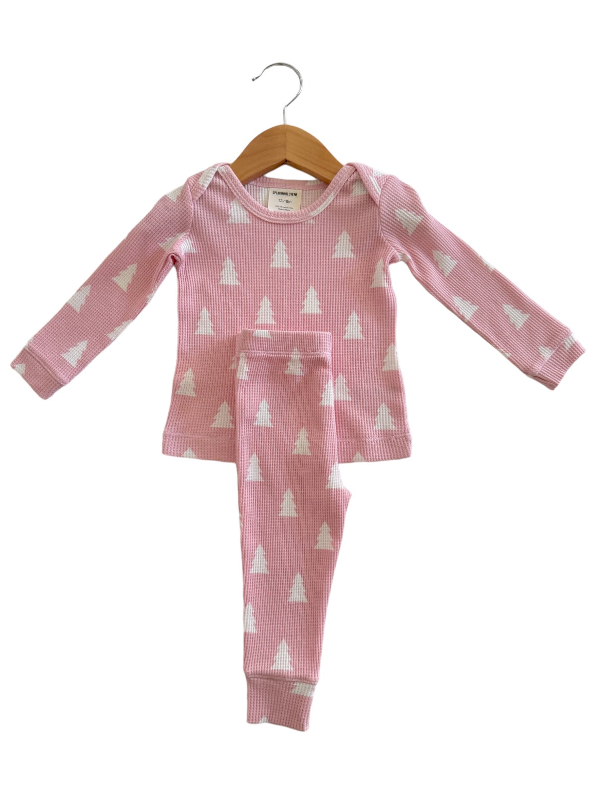 Pink children's pajamas with white tree patterns, hanging on a wooden hanger.