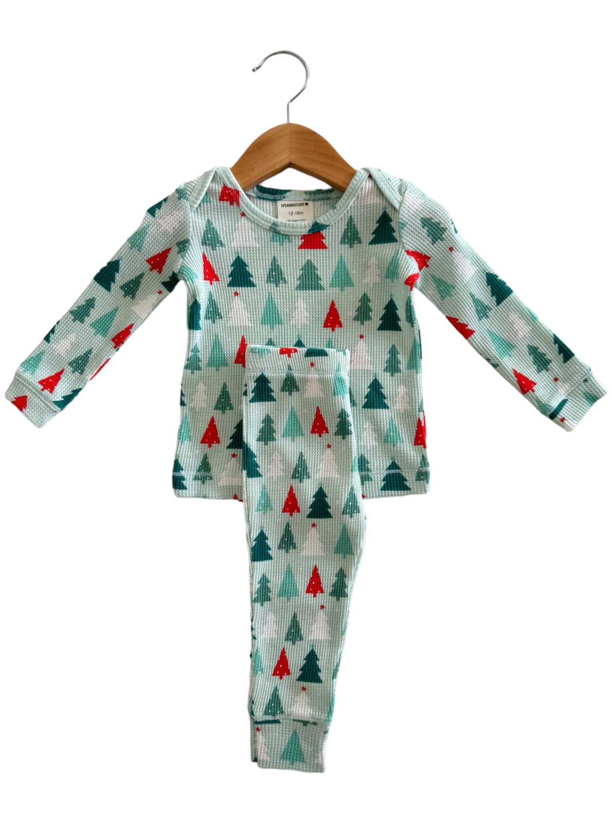 Children's pajamas featuring a holiday tree pattern in green and red, hanging on a wooden hanger.