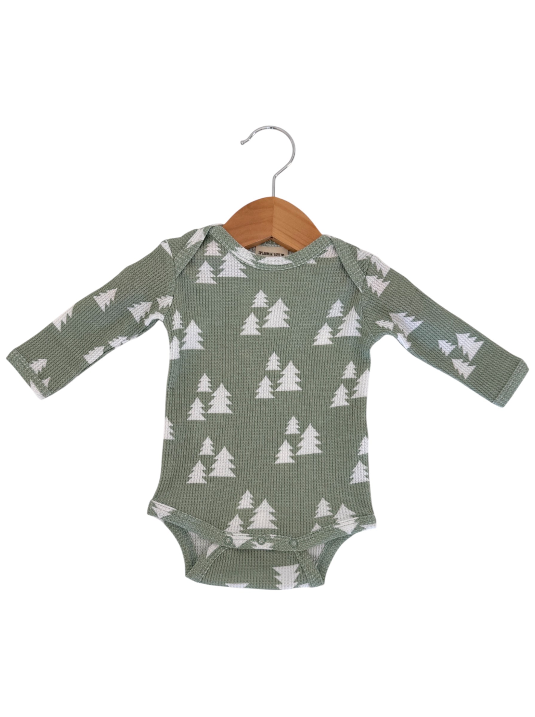Green long-sleeve onesie with white tree pattern, hanging on a wooden hanger.