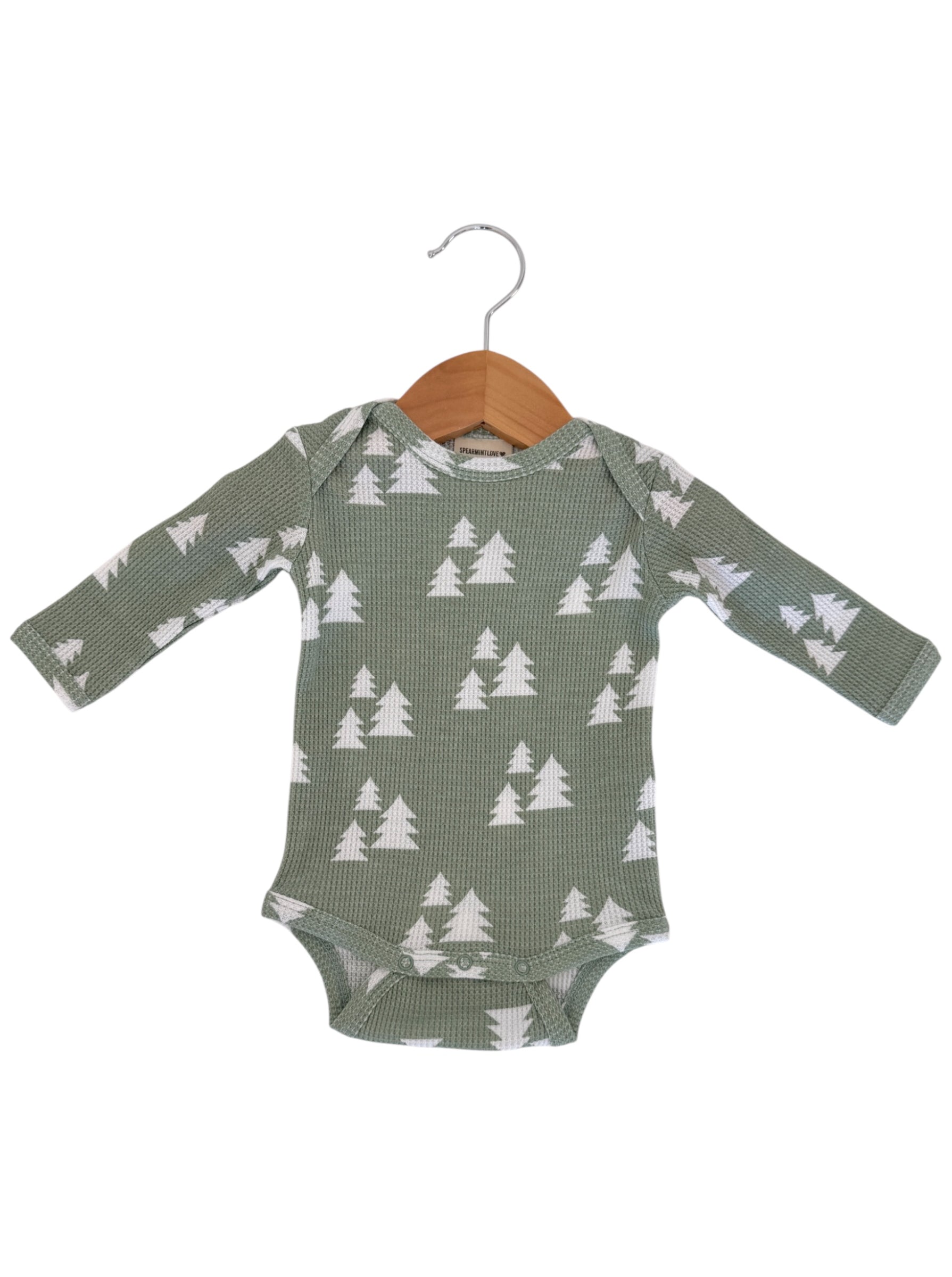 Green long-sleeve onesie with white tree pattern, hanging on a wooden hanger.