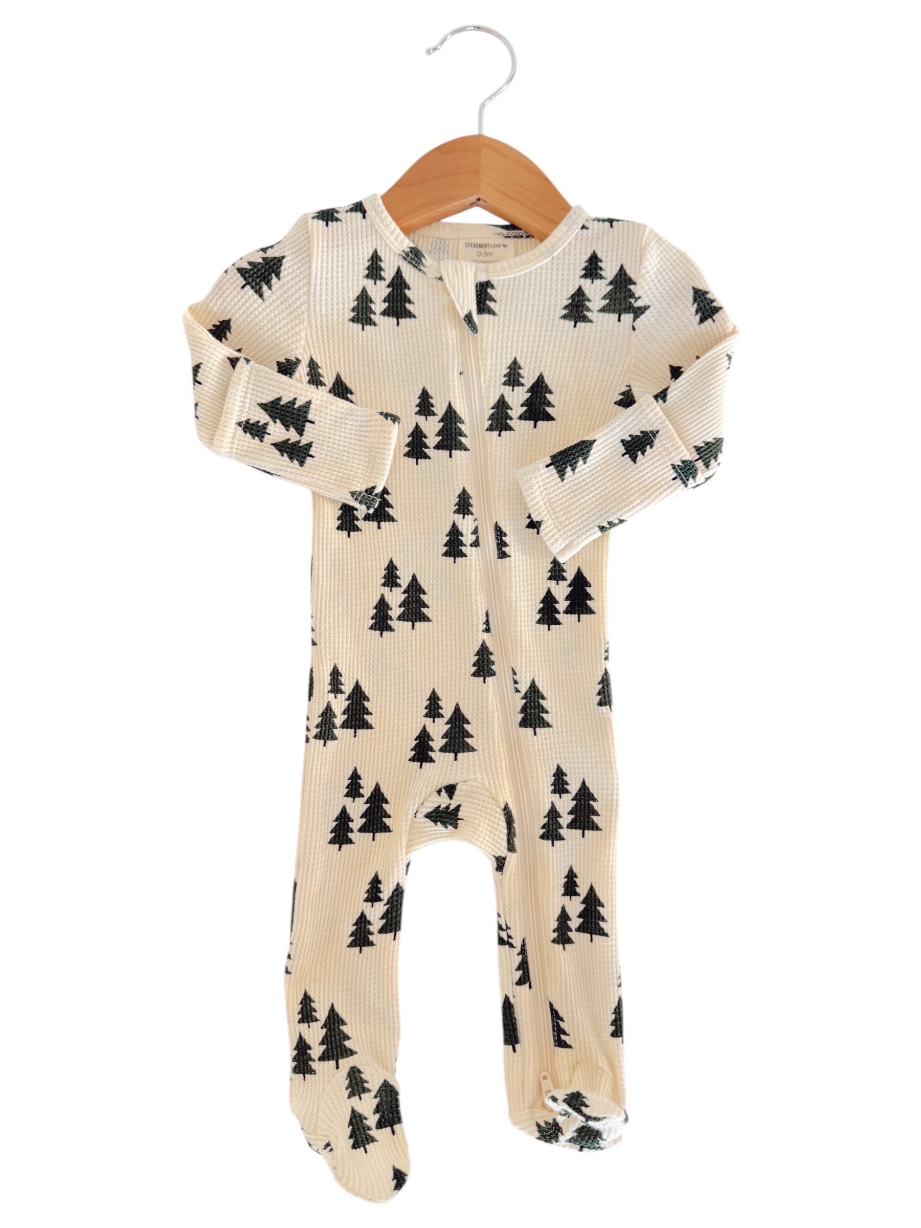 Cream-colored baby onesie with black tree print, displayed on a wooden hanger.