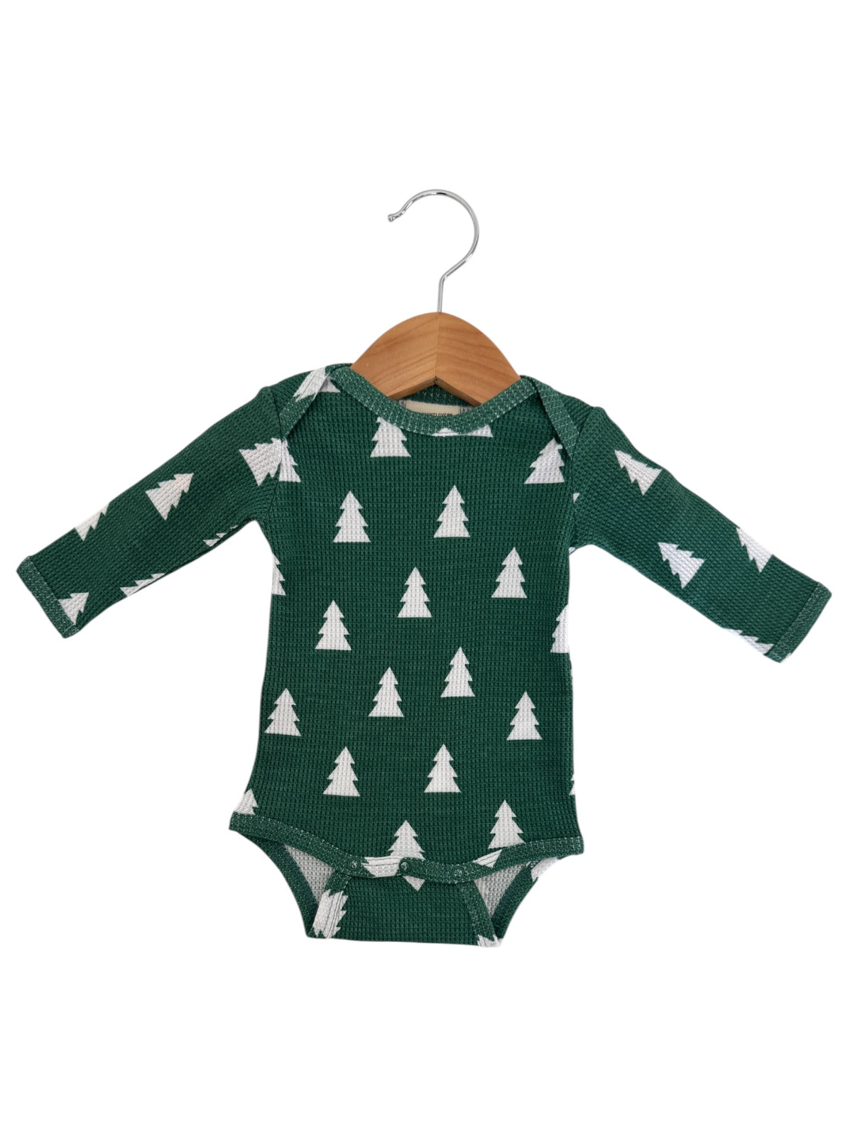 Green baby onesie with white tree patterns, displayed on a wooden hanger against a white background.