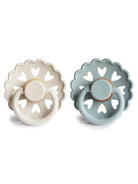 Two silicone pacifiers in white and blue with heart cutouts, designed for babies. Brand: Frigg.