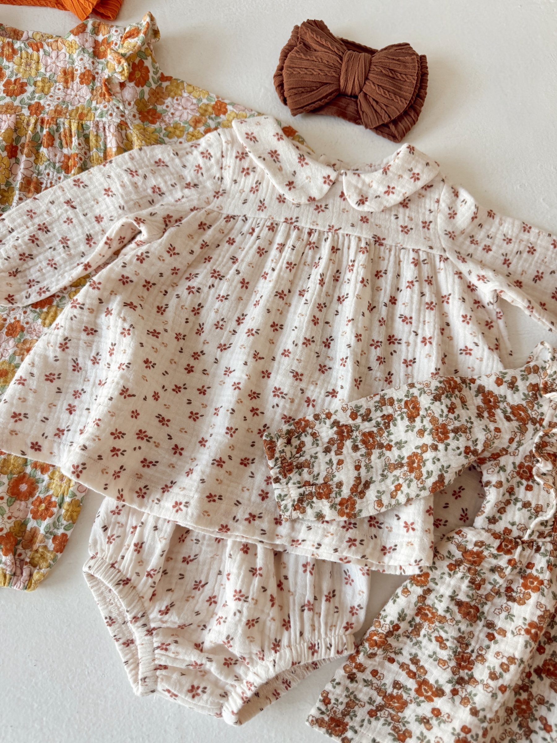 Floral children's clothing set including a top, bloomers, and hair bow on a light background.