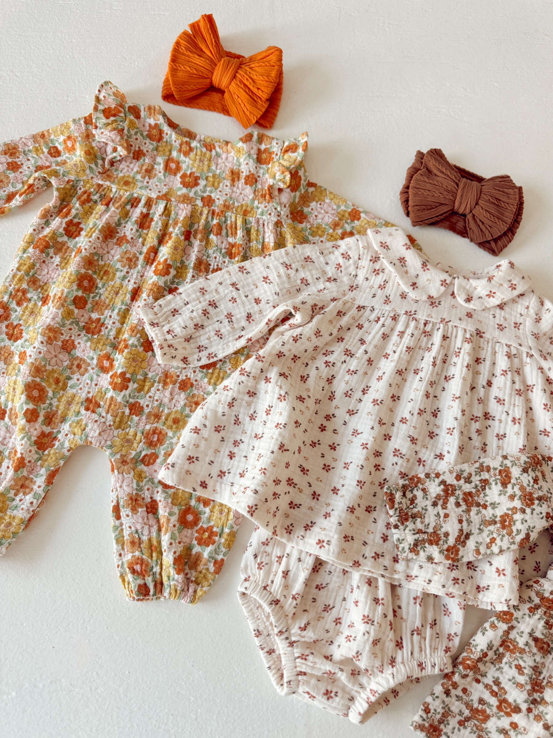 Variety of children's clothing with floral prints and bow accessories in orange and brown on a white background.