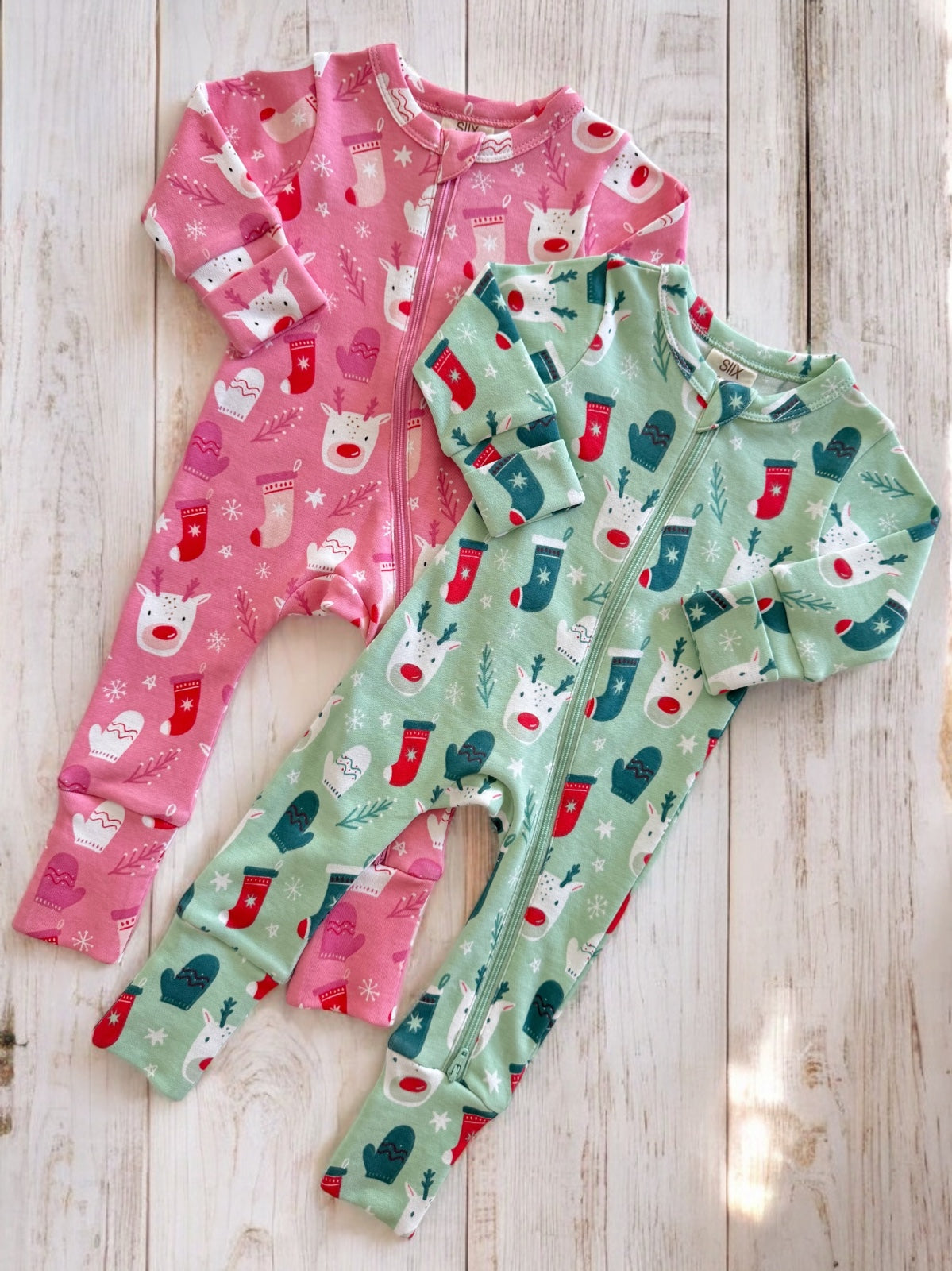 Two colorful children's onesies in pink and green with festive designs, on a light wooden background.