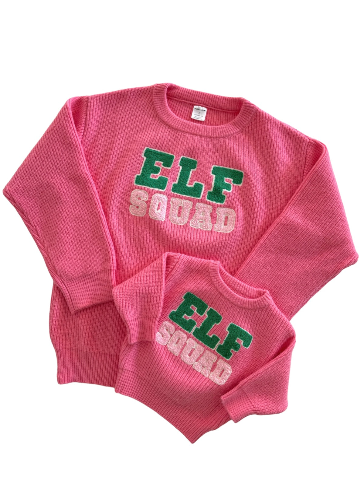 Matching pink "Elf Squad" sweaters for adults and kids, featuring textured fabric and colorful lettering.