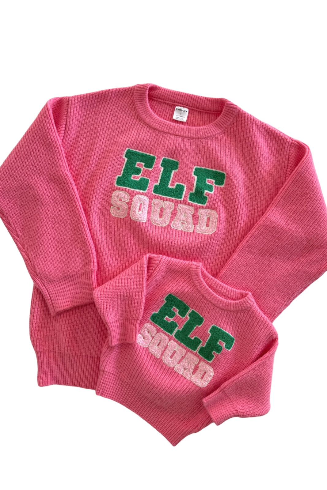 Matching pink "Elf Squad" sweaters for adults and kids, featuring textured fabric and colorful lettering.