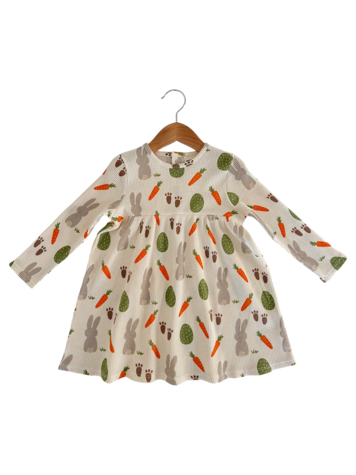 Baby dress with bunny, carrot, and cactus patterns, hanging on a wooden hanger against a white background.