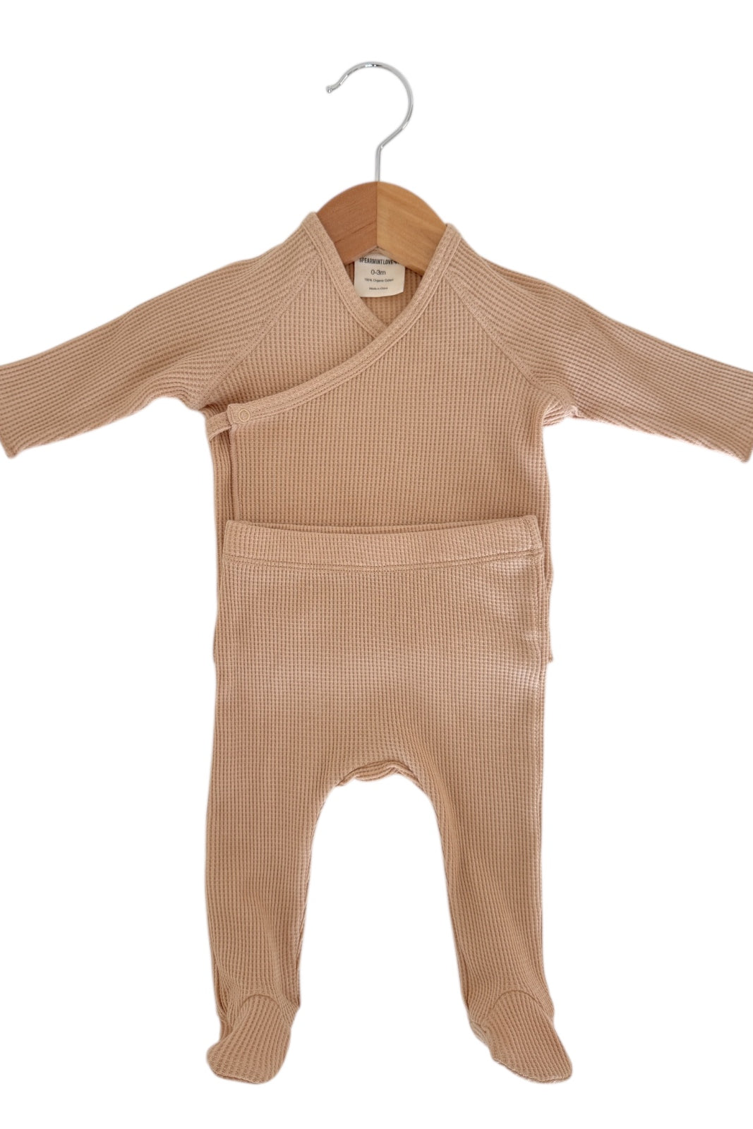 Light beige baby outfit displayed on a wooden hanger, featuring long sleeves and footed pants.