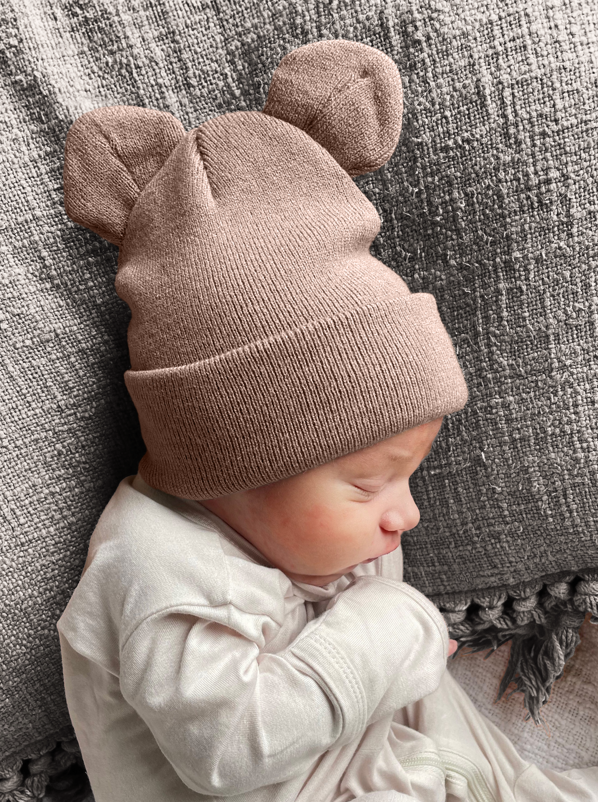 Baby wearing a soft, brown bear-ear hat, resting on textured fabric.