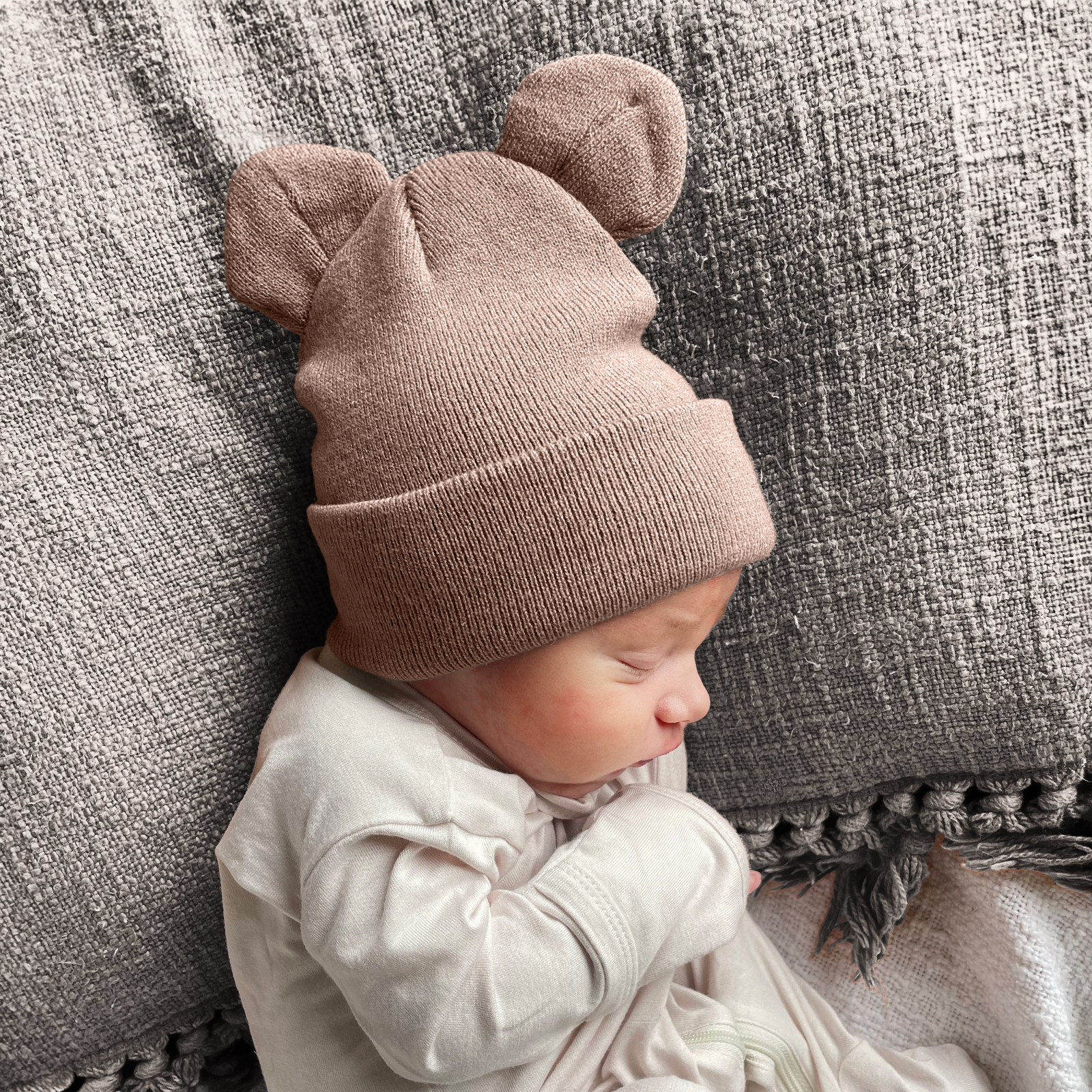 Baby wearing a soft, brown bear-ear hat, resting on textured fabric.