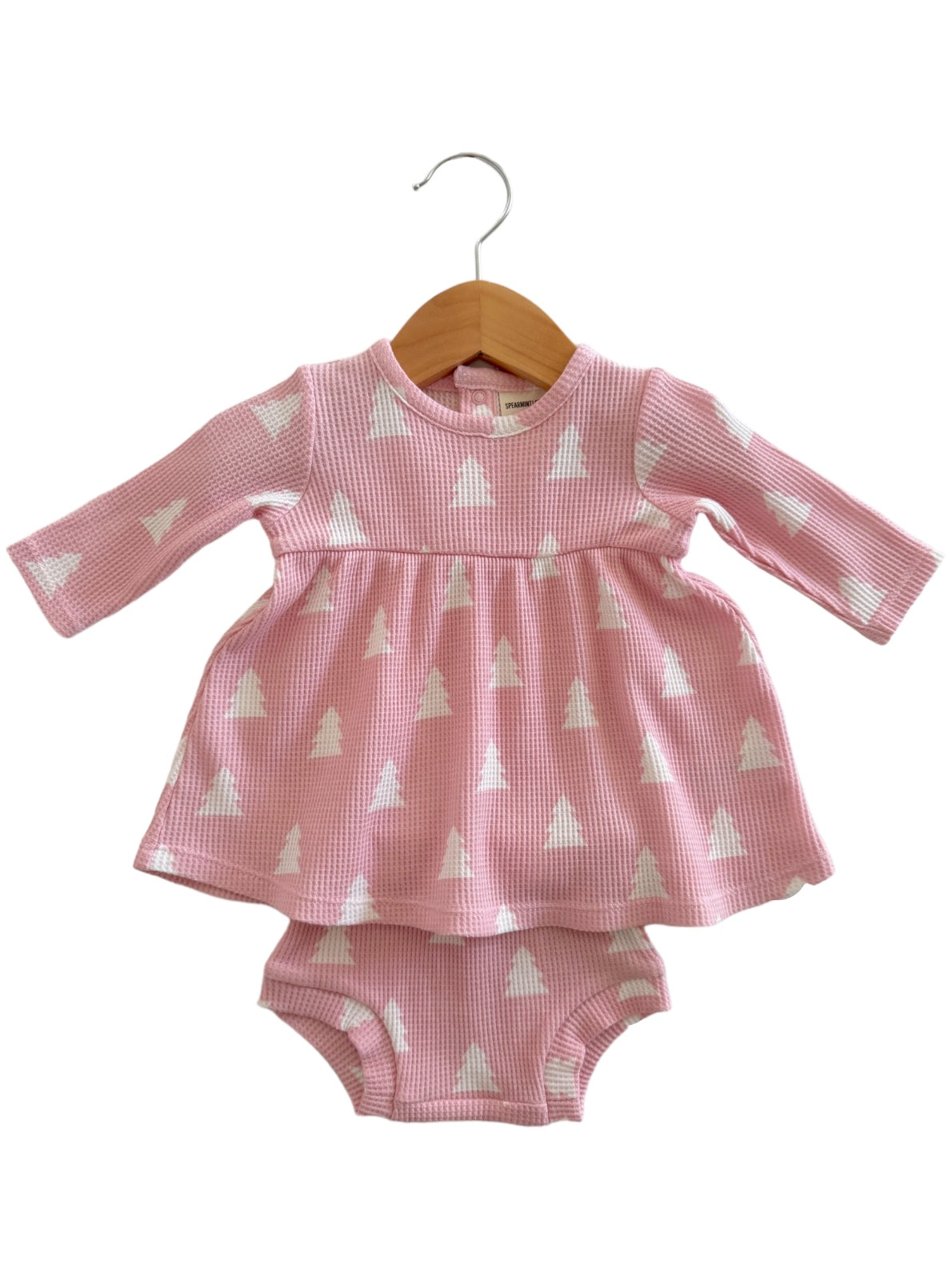 Pink dress with long sleeves and white triangle patterns, hanging on a wooden hanger, paired with a matching diaper cover.