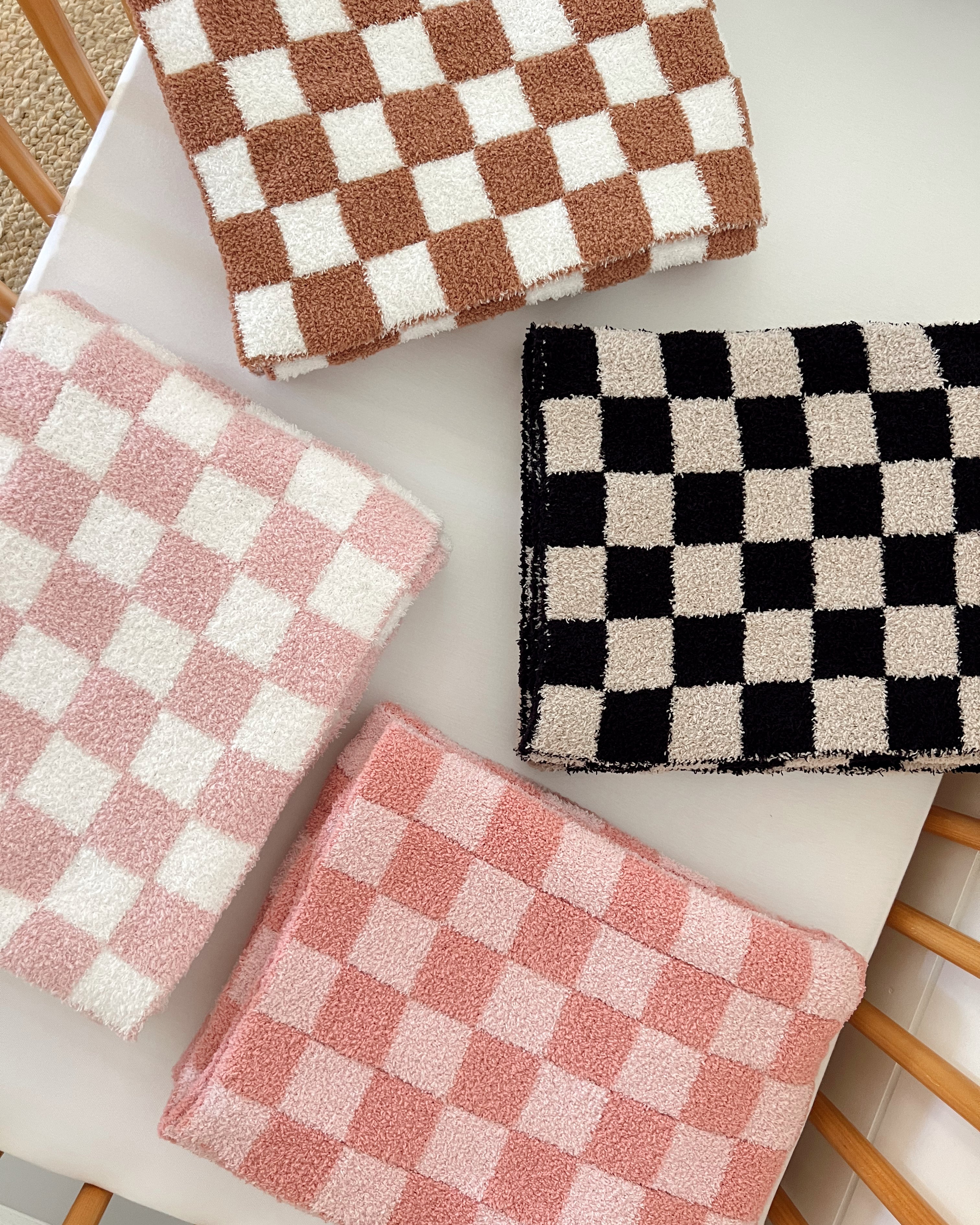 Four textured checkered towels in pink, brown, black, and white arranged on a light surface.