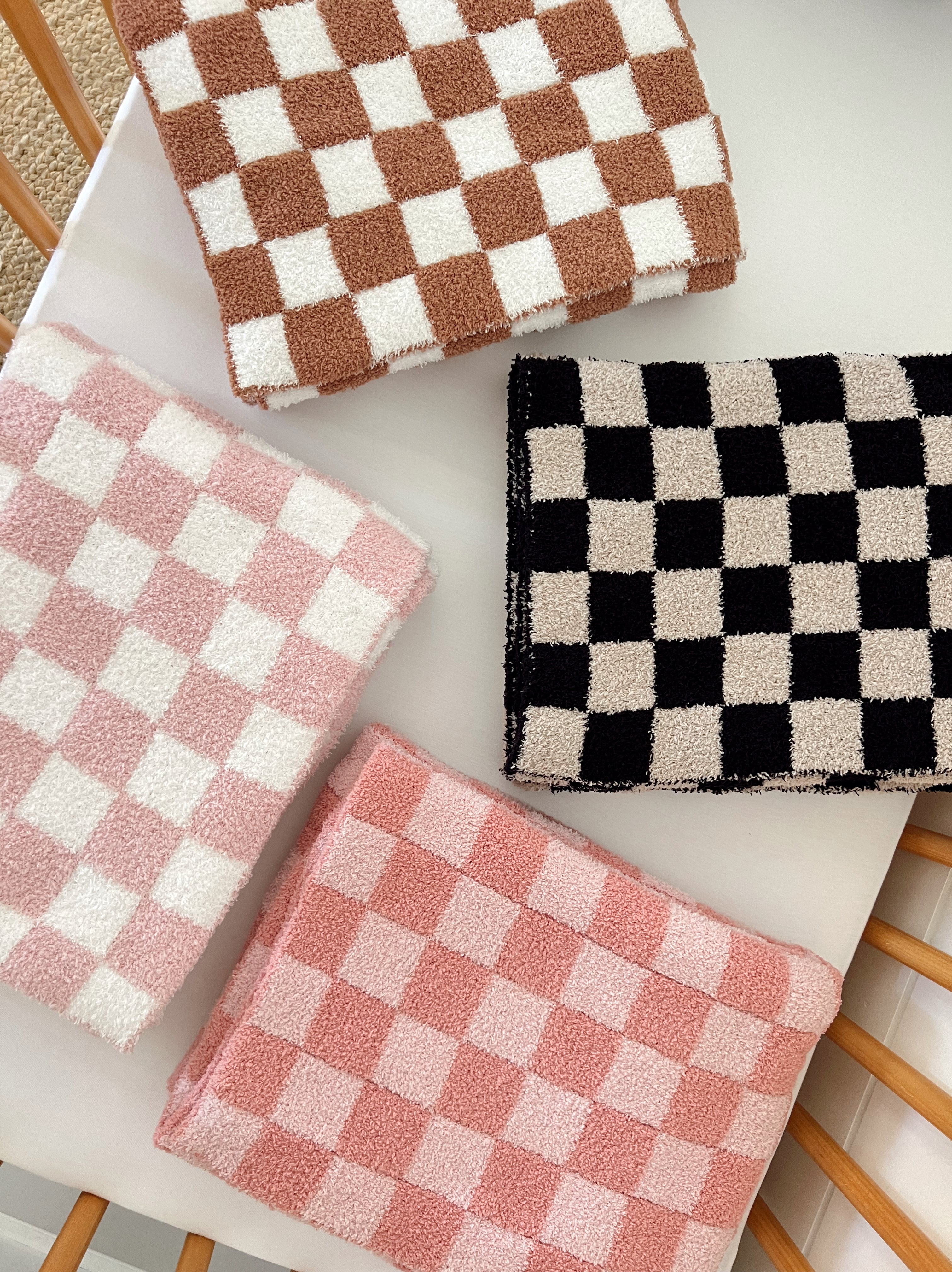 Four textured checkered towels in pink, brown, black, and white arranged on a light surface.
