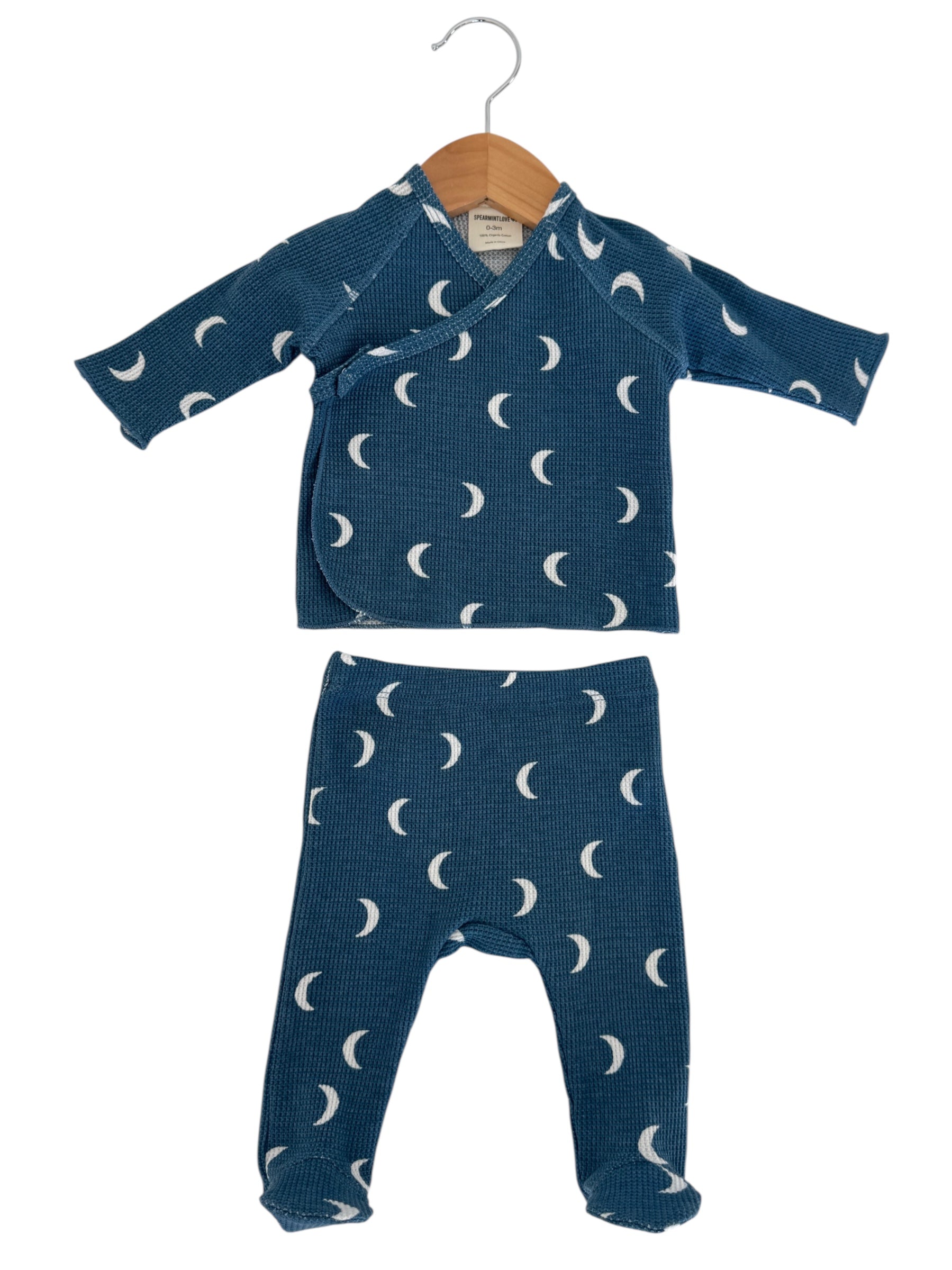 Blue baby outfit with moon patterns, featuring a wrap-style top and matching pants, displayed on a hanger.