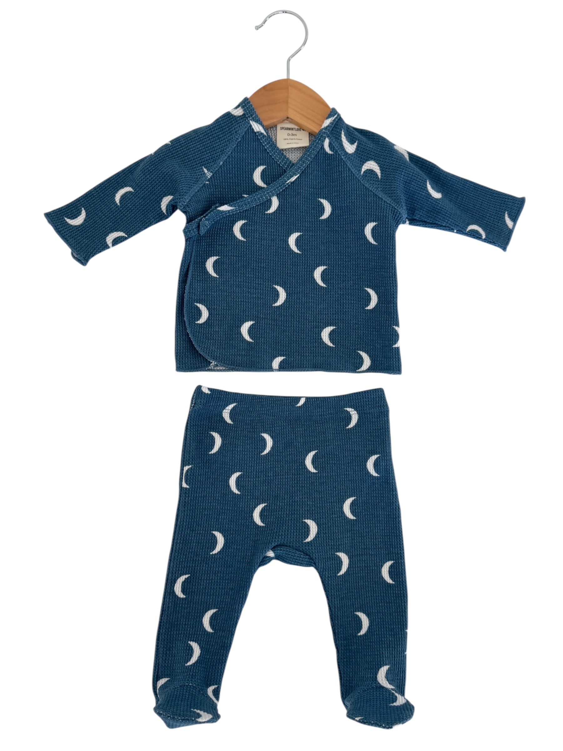 Blue baby outfit with moon patterns, featuring a wrap-style top and matching pants, displayed on a hanger.