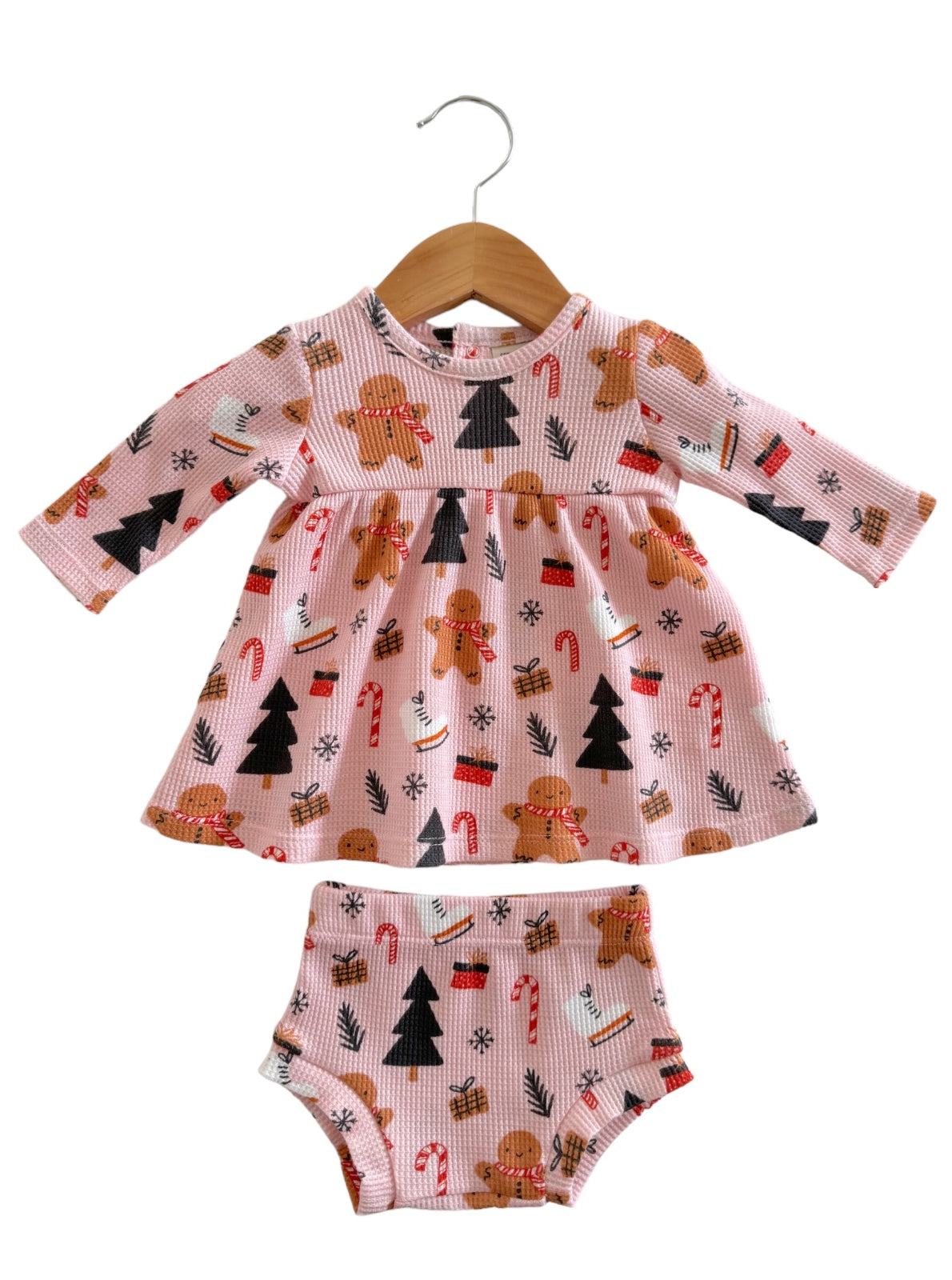 Pink toddler dress with gingerbread and Christmas patterns, paired with matching bloomers, hanging on a wooden hanger.