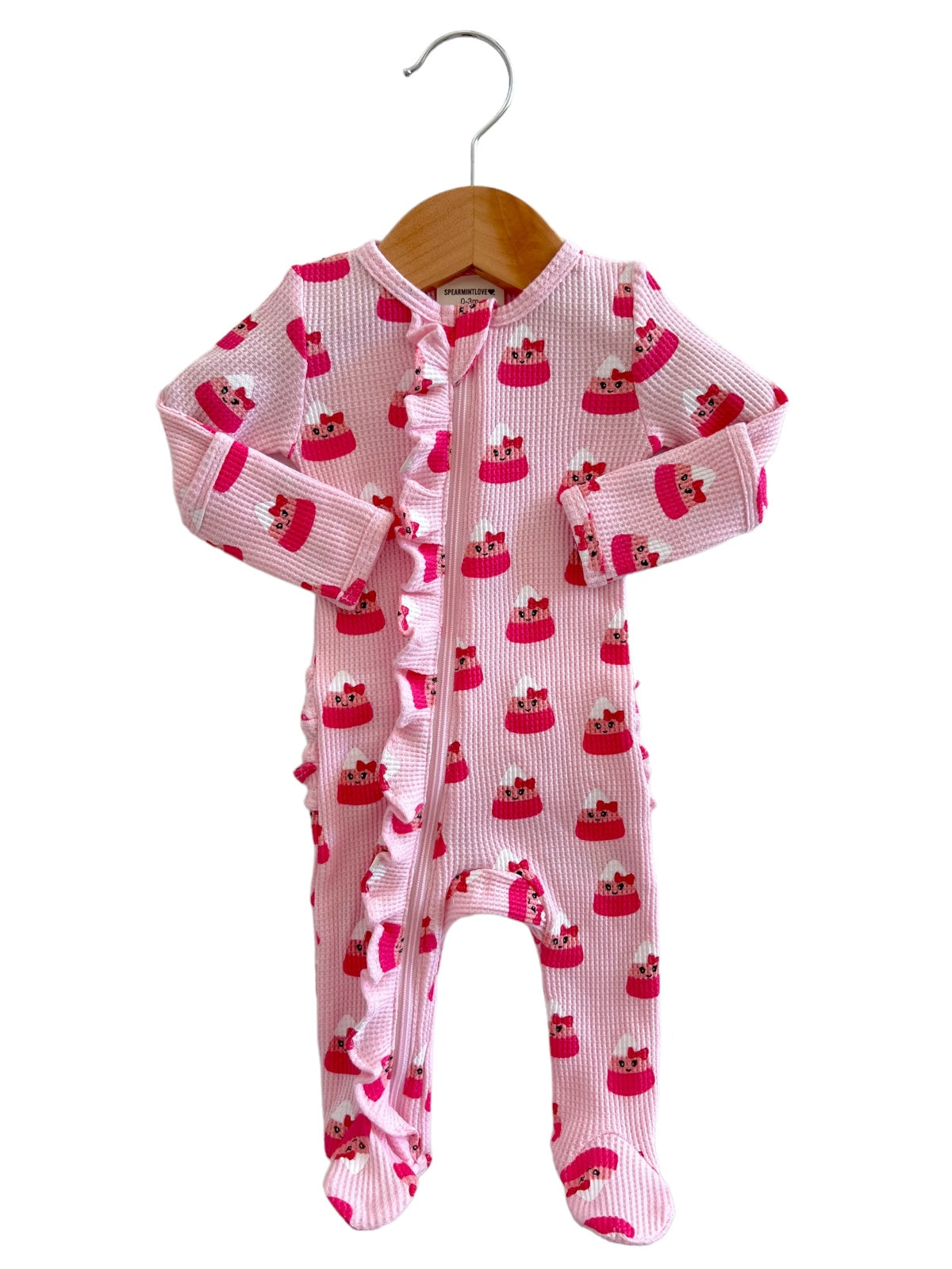 Pink baby onesie with cake print, featuring ruffles, hanging on a wooden hanger.