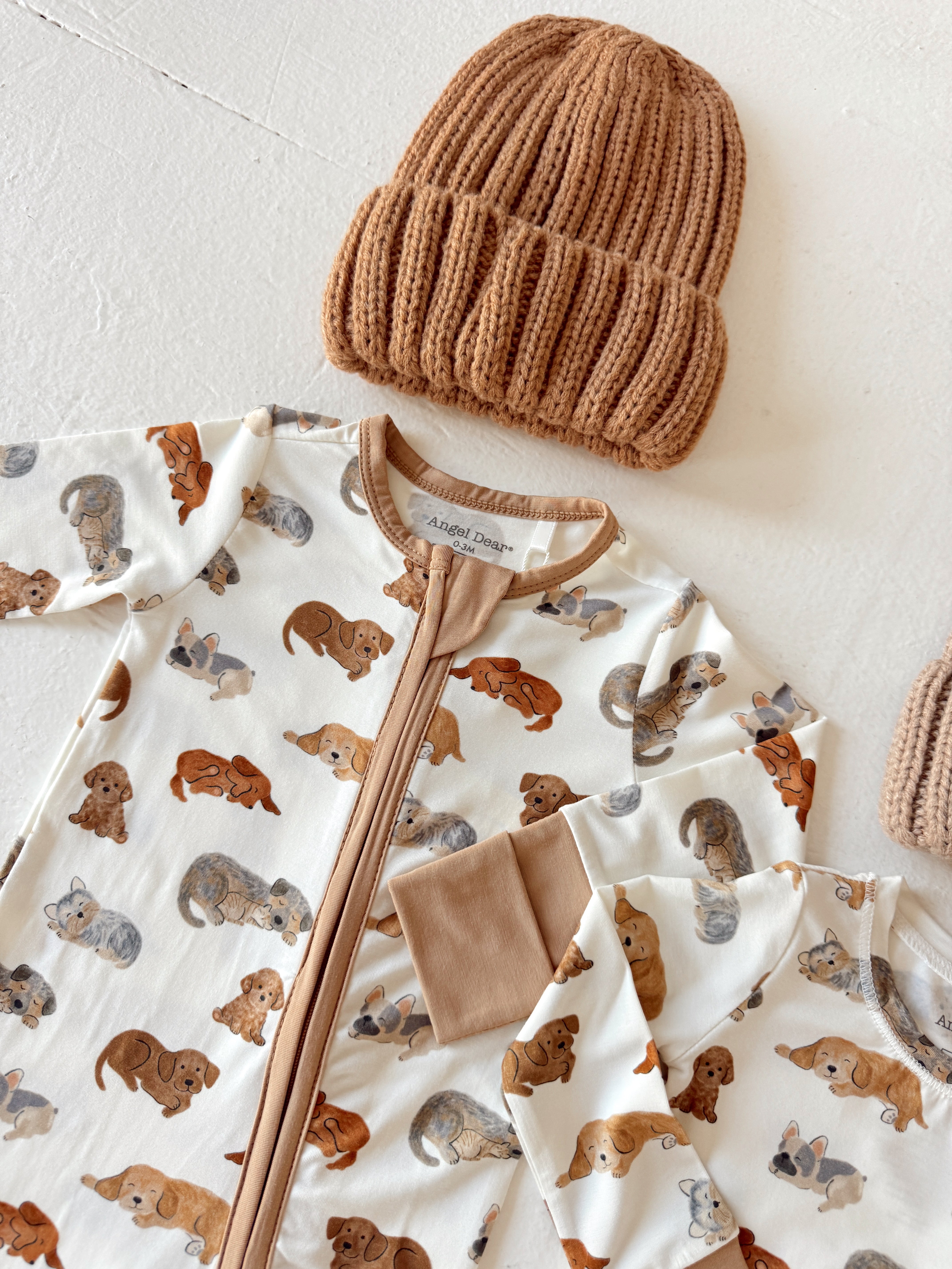Tan knitted beanie and cream pajamas with playful dog prints lay on a white surface.