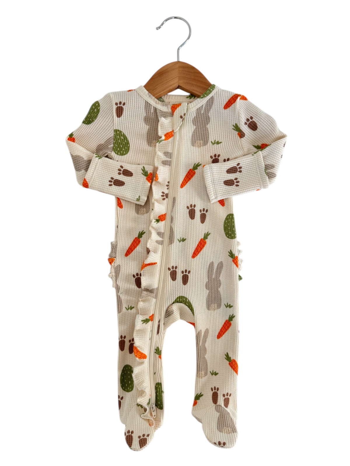 Infant onesie with bunny and carrot patterns, featuring a front zipper and ruffled trim, displayed on a hanger.