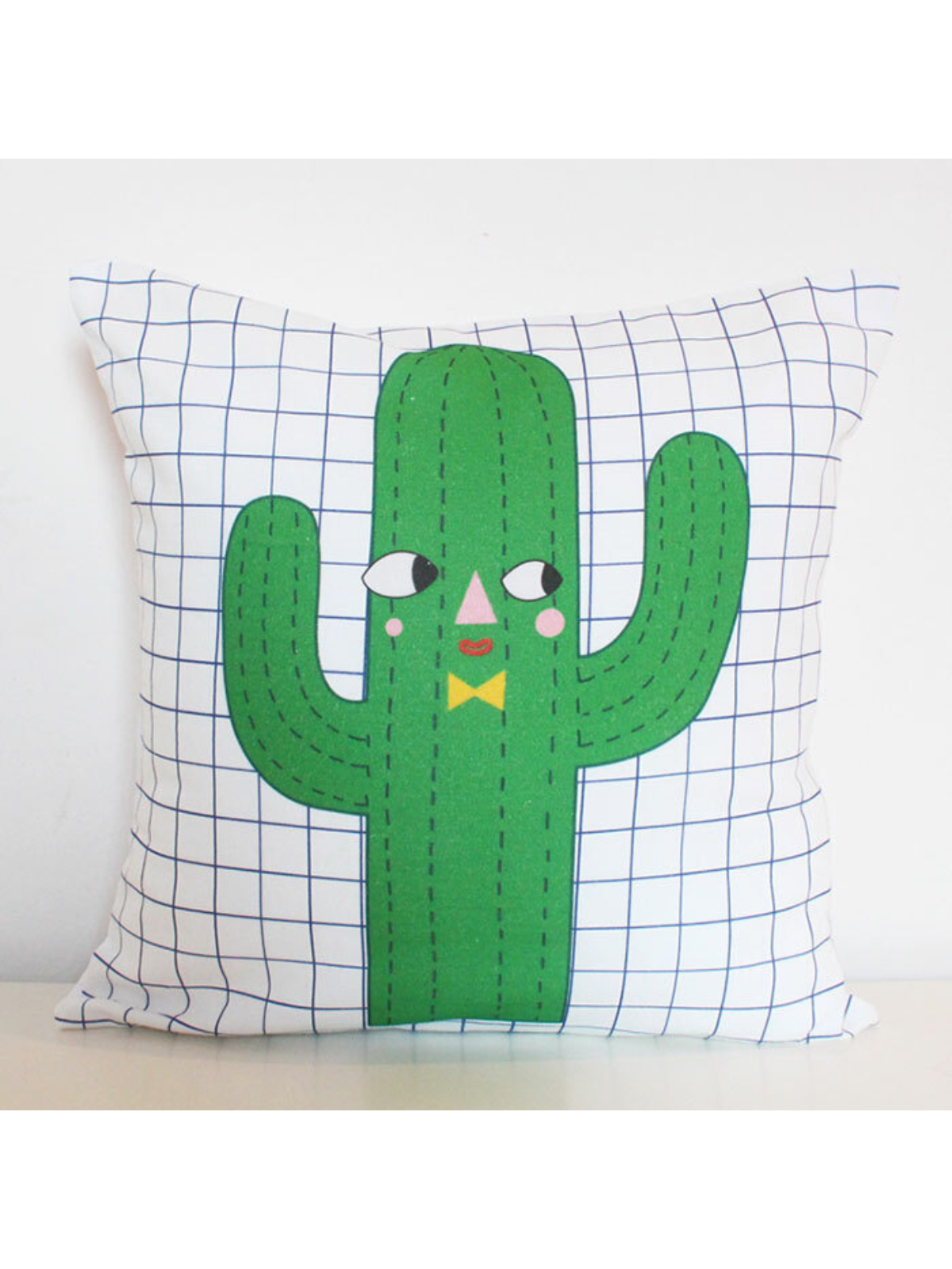 Green cactus pillow with a smiling face on a grid pattern background. Fun and whimsical design for decor.