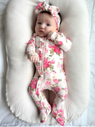 Baby girl in floral onesie with a matching headband, lying on a soft, cream-colored surface.