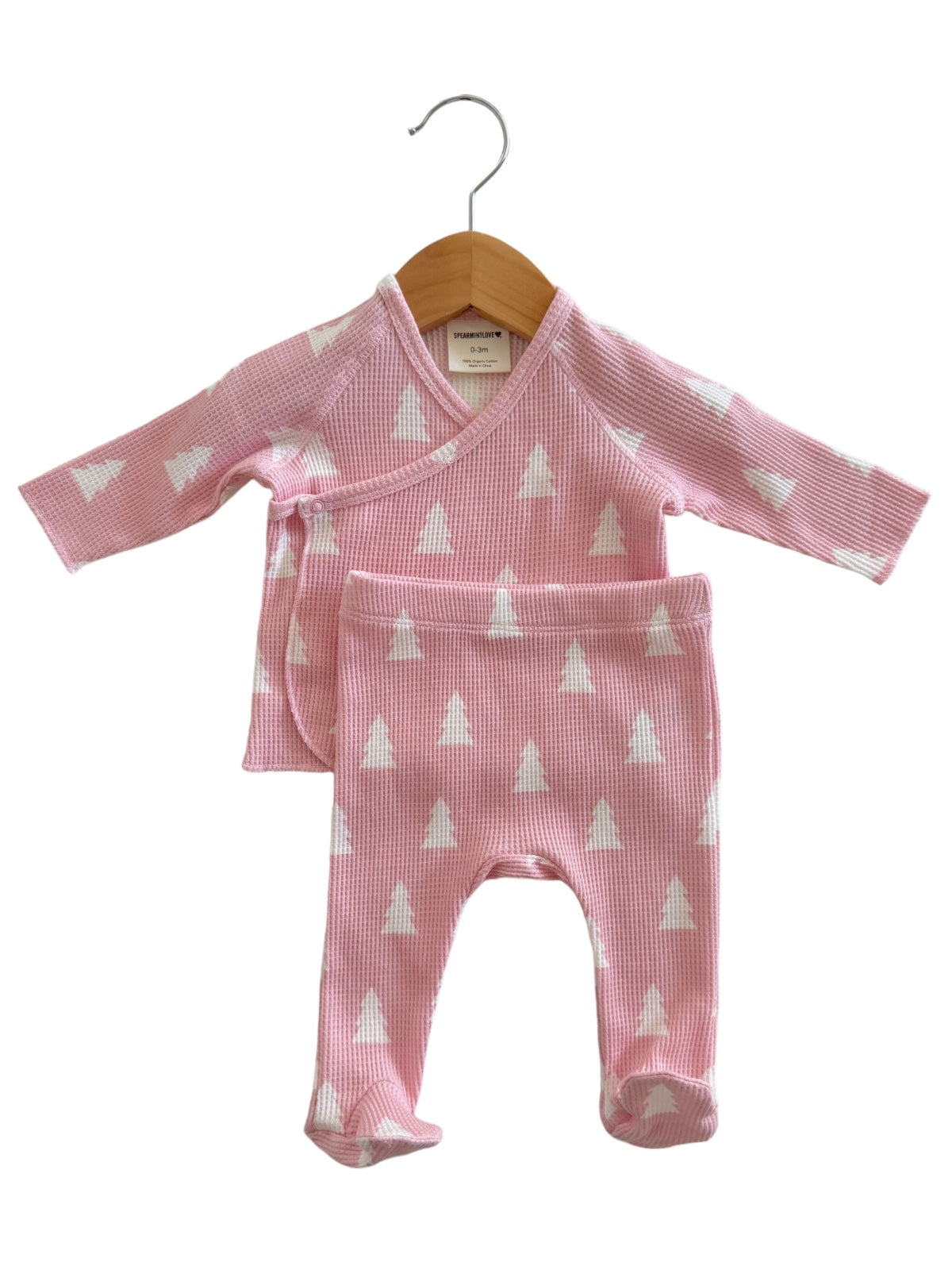 Pink baby outfit with a wrap top and matching pants, featuring white tree patterns, hanging on a wooden hanger.
