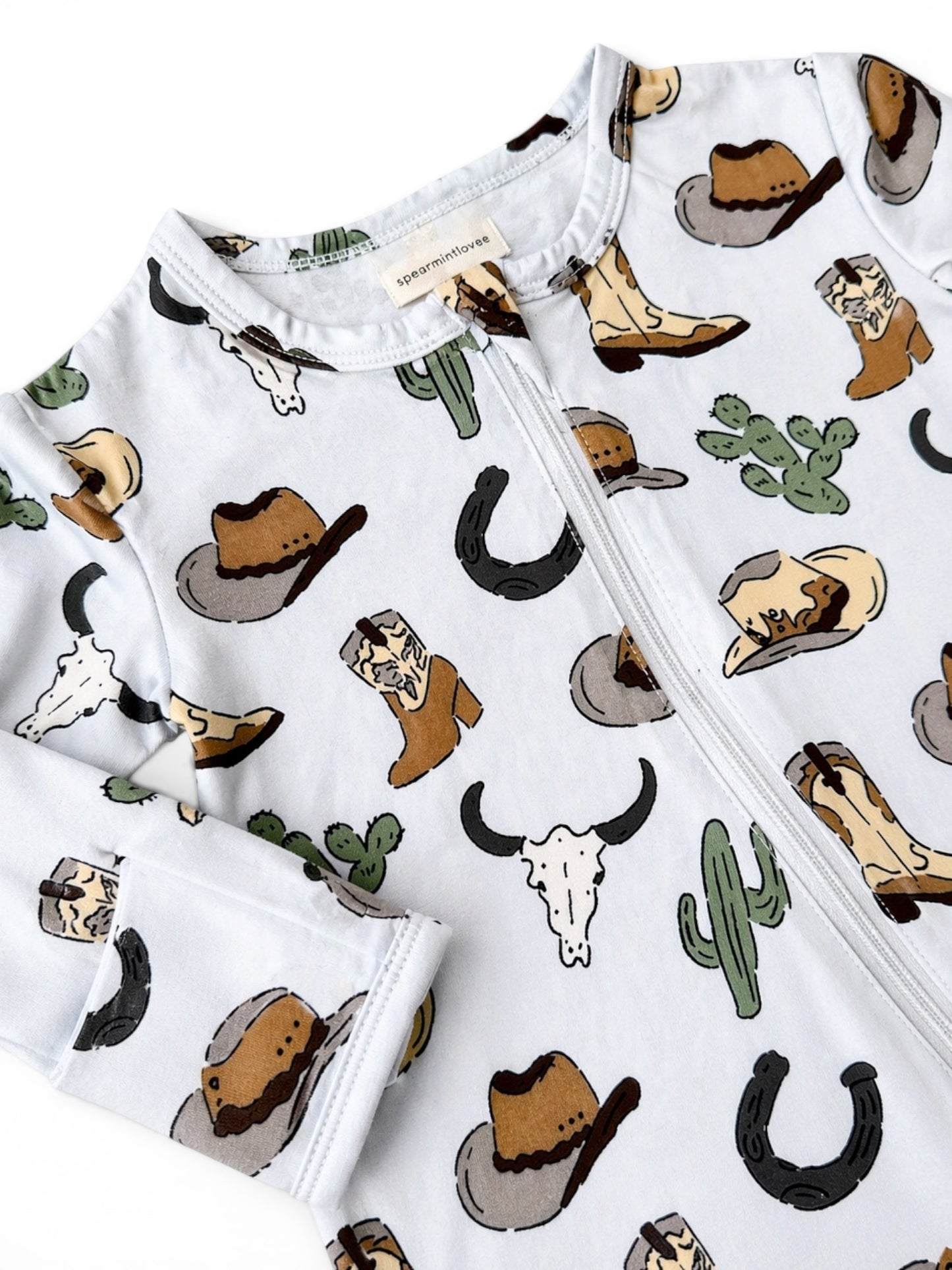 Cowboy-themed baby onesie featuring hats, boots, cacti, and western motifs on a light background.