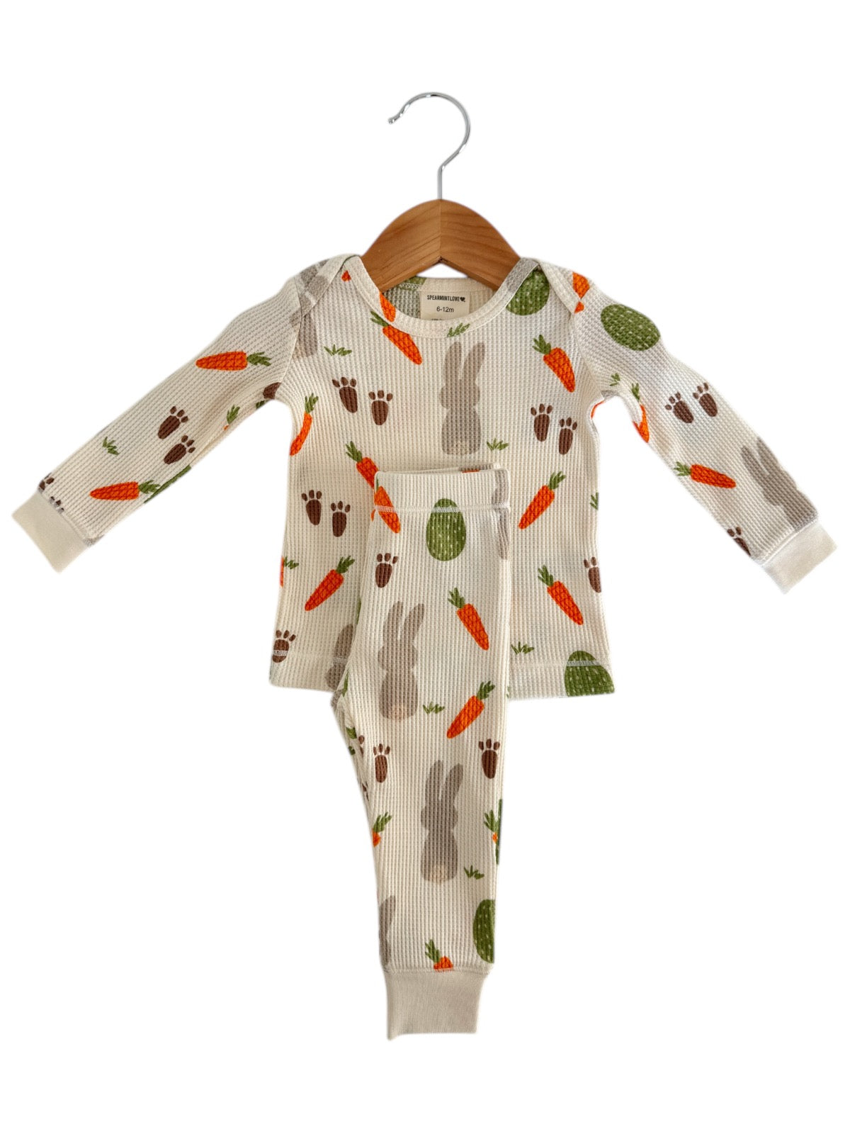 Child's ribbed pajama set with bunny, carrot, and cactus patterns, hanging on a wooden hanger.