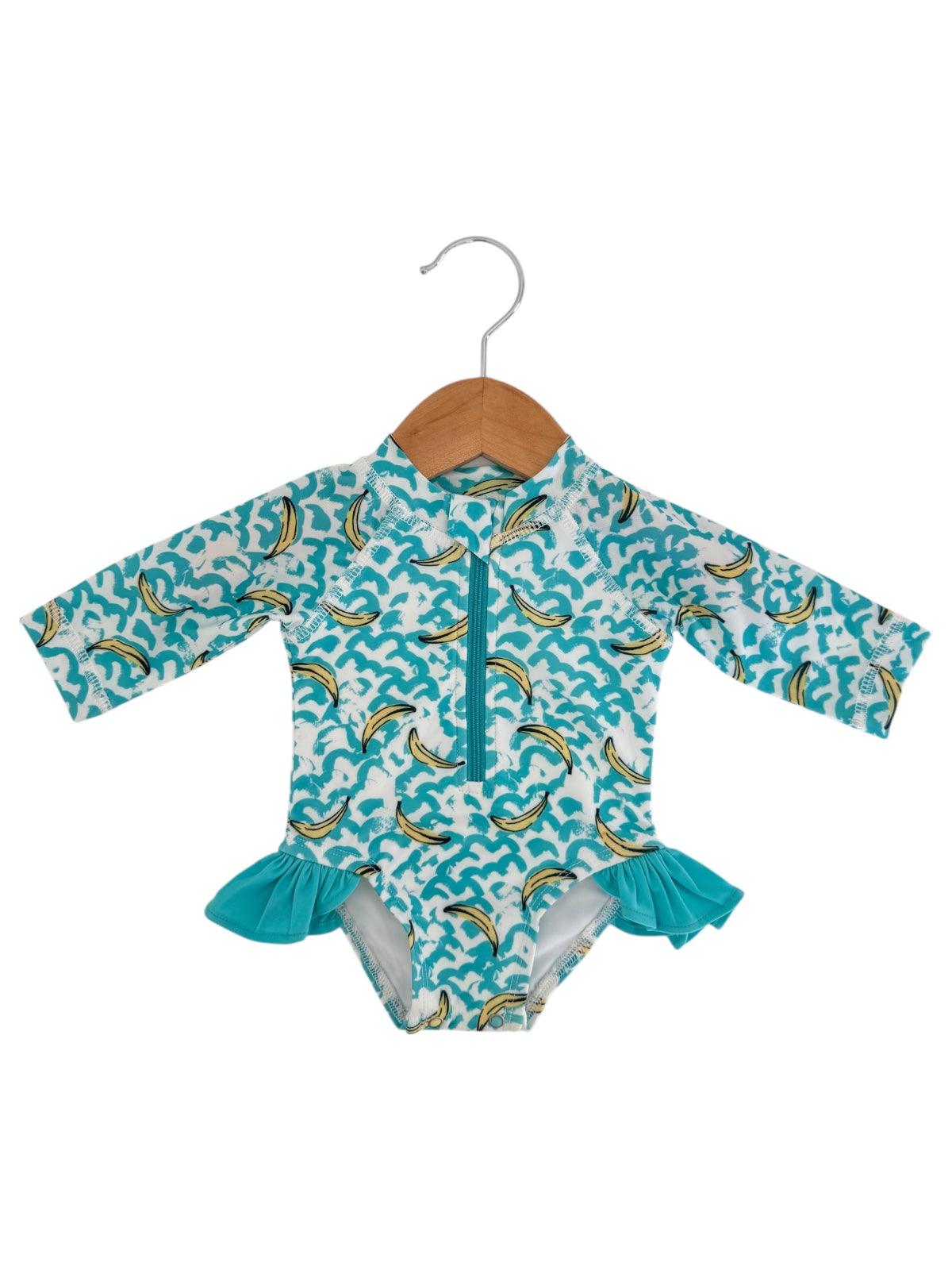 Colorful long-sleeve swimsuit with banana and wave patterns, featuring a ruffled bottom, displayed on a hanger.