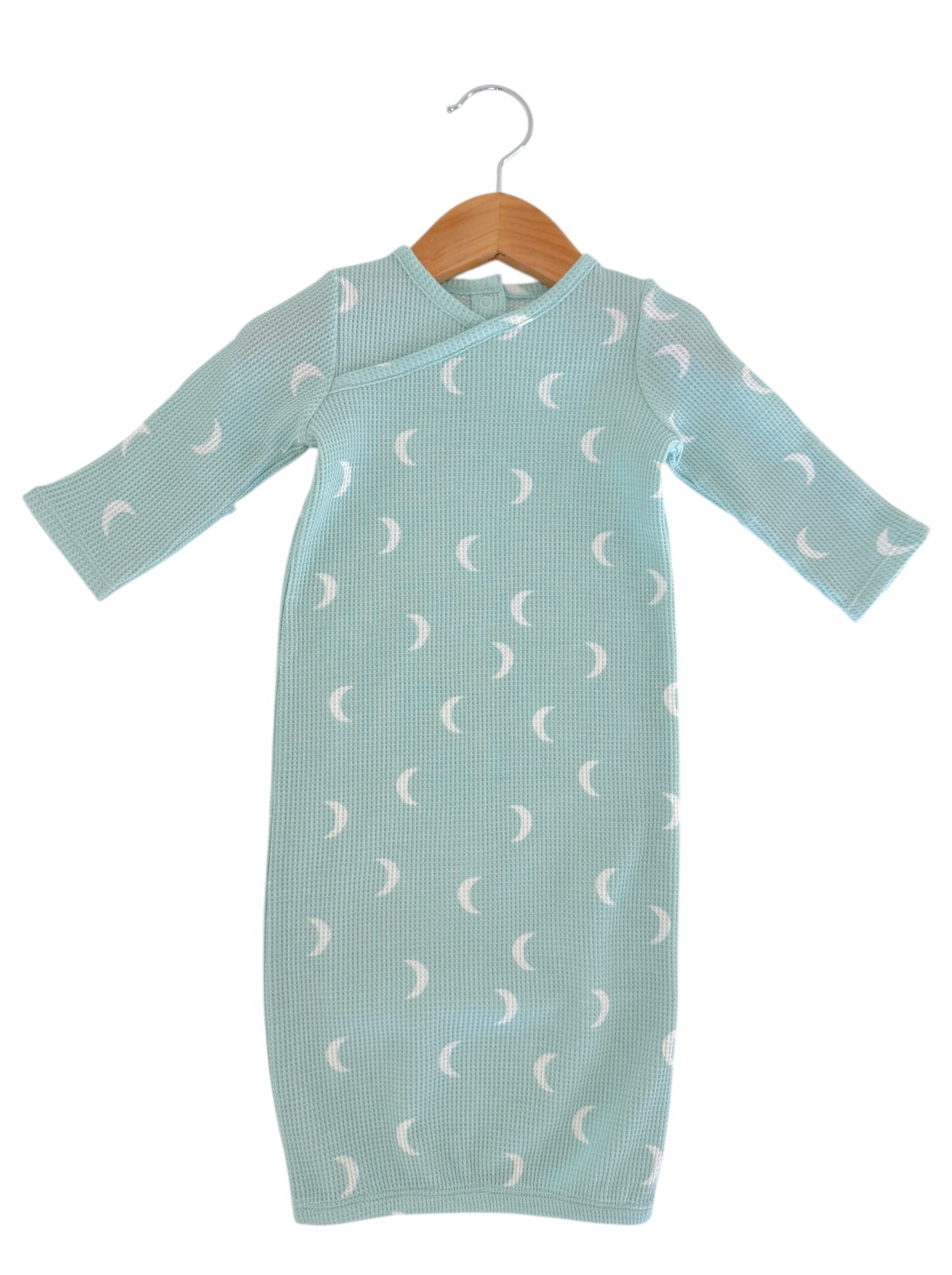 Light blue baby dress with moon patterns, hanging on a wooden hanger.