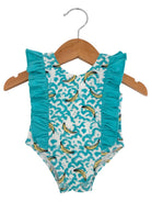 Turquoise baby swimsuit with ruffles and banana print, hanging on a wooden hanger.