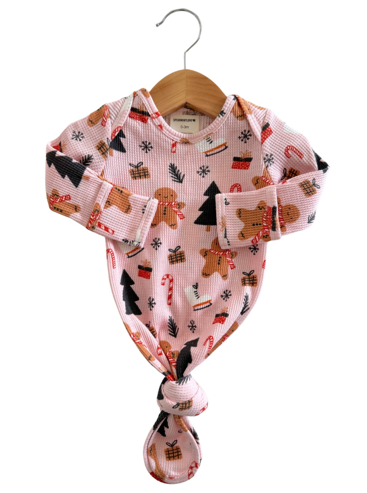 Infant bodysuit with gingerbread and Christmas-themed prints hanging on a wooden hanger against a white background.