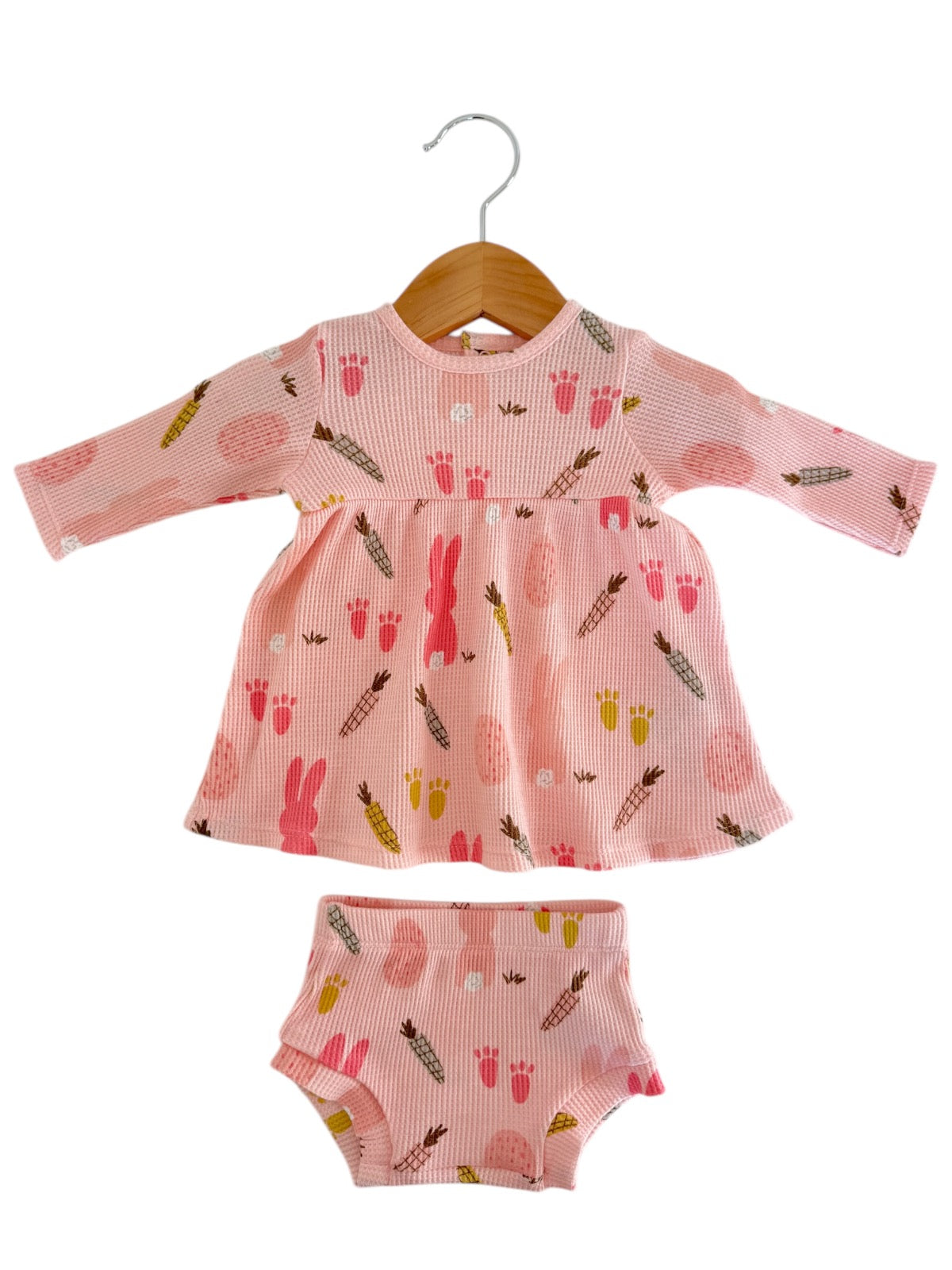 Pink toddler dress and matching shorts with colorful bunny and ice cream prints on a wooden hanger.