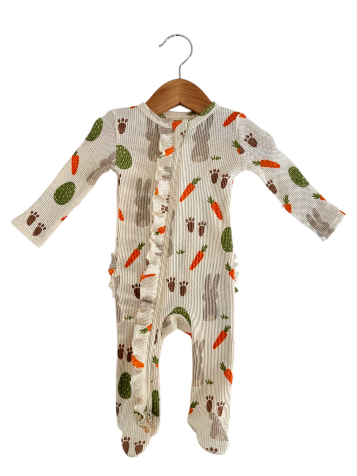 Baby onesie with bunny and carrot print, features ruffles and a front zipper, hanging on a wooden hanger.