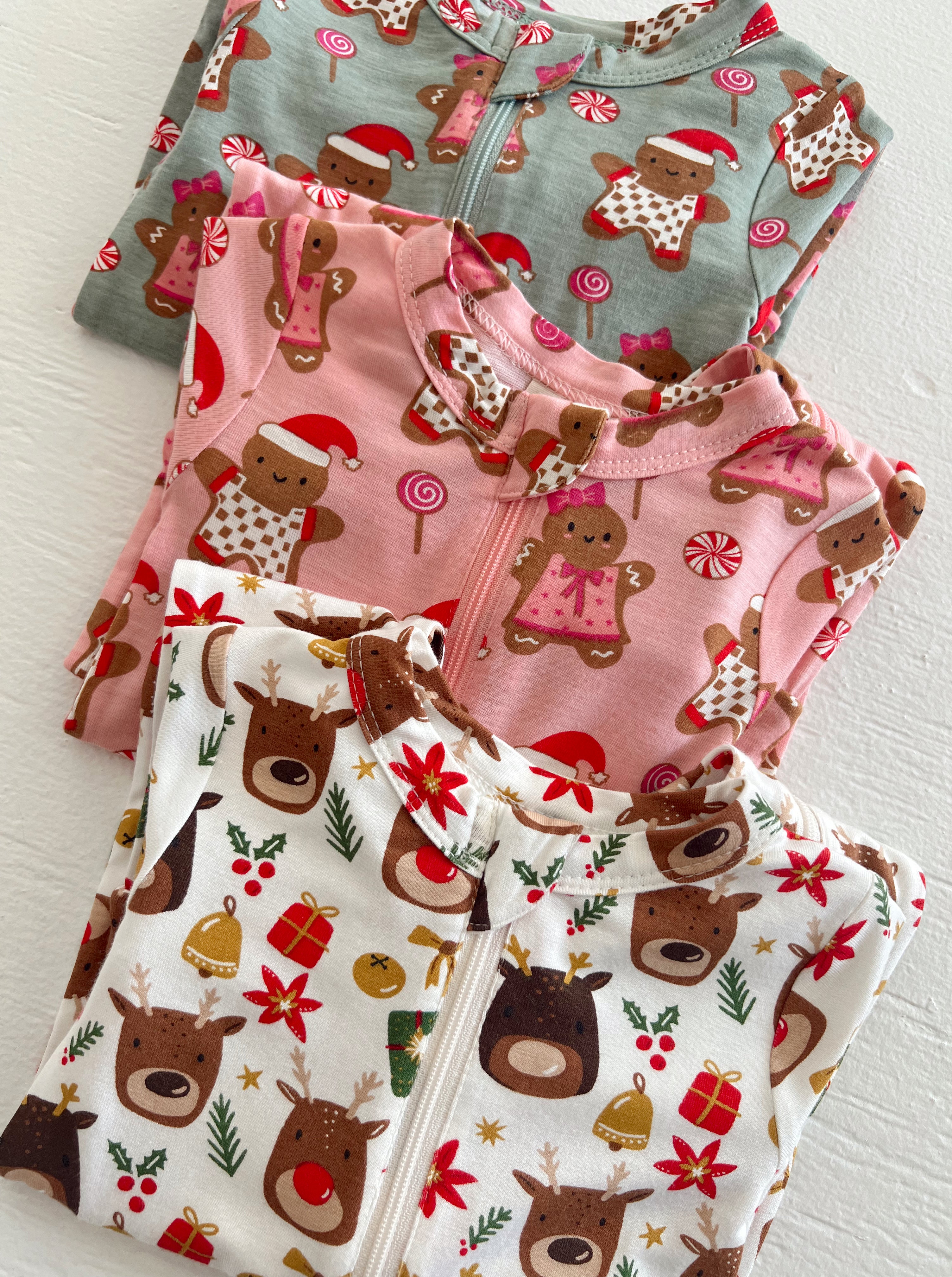 Three festive children's pajamas with gingerbread and reindeer designs in pink, gray, and white.