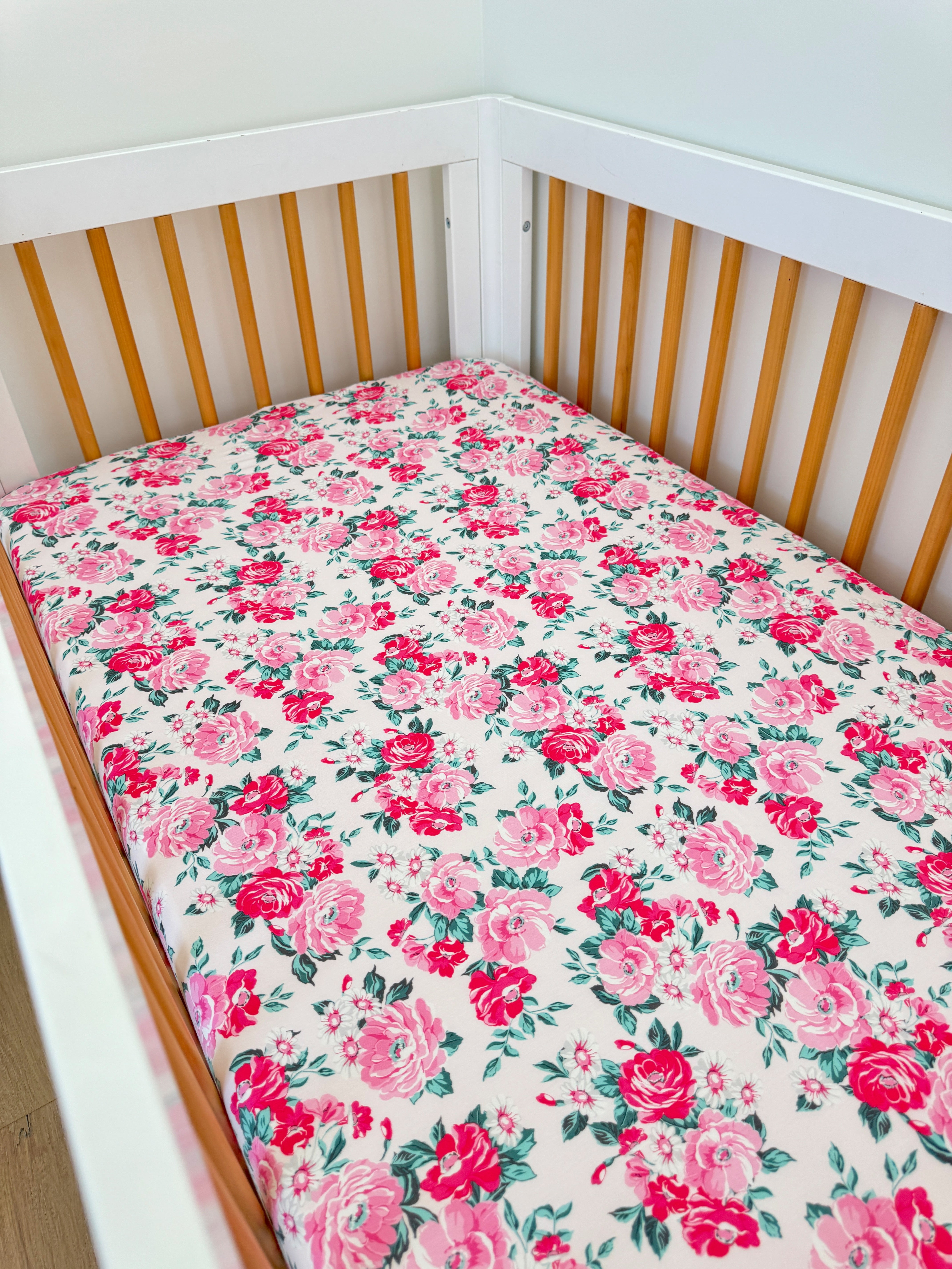 White crib with floral-patterned mattress featuring pink roses on a light background.