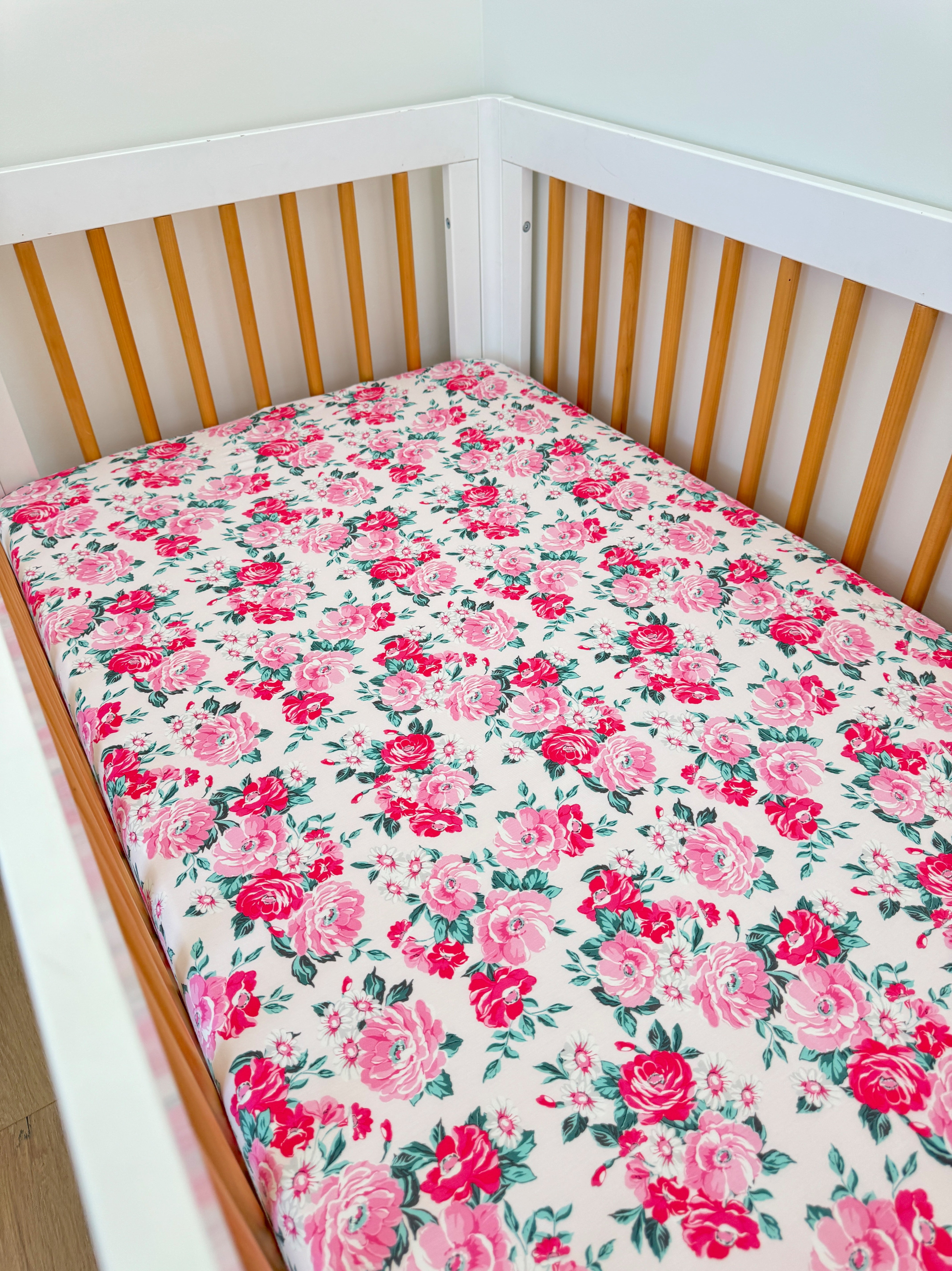 White crib with floral-patterned mattress featuring pink roses on a light background.